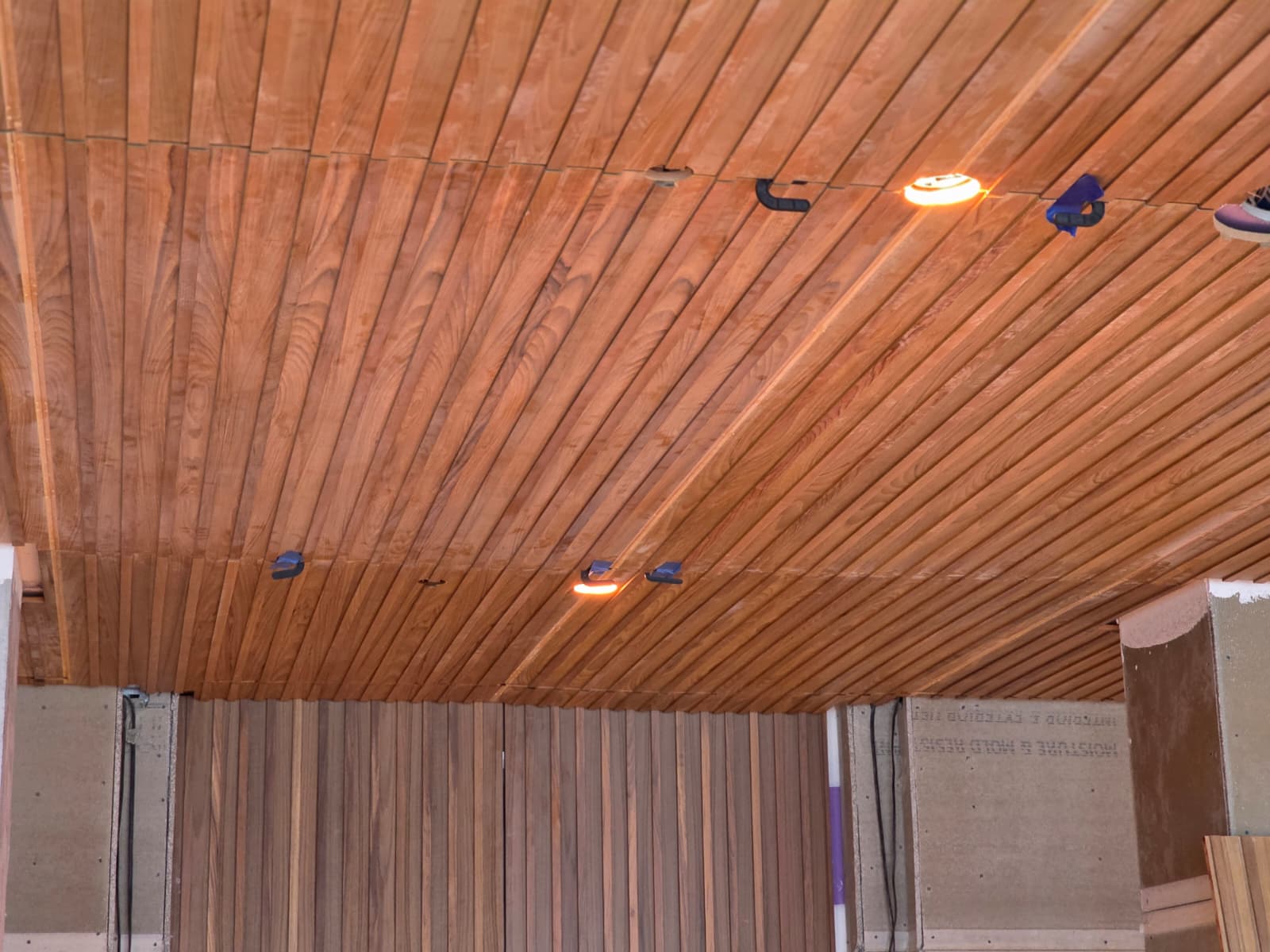 Warm linear wood plank ceiling installation with active clamps and warm recessed lighting in Greensboro NC