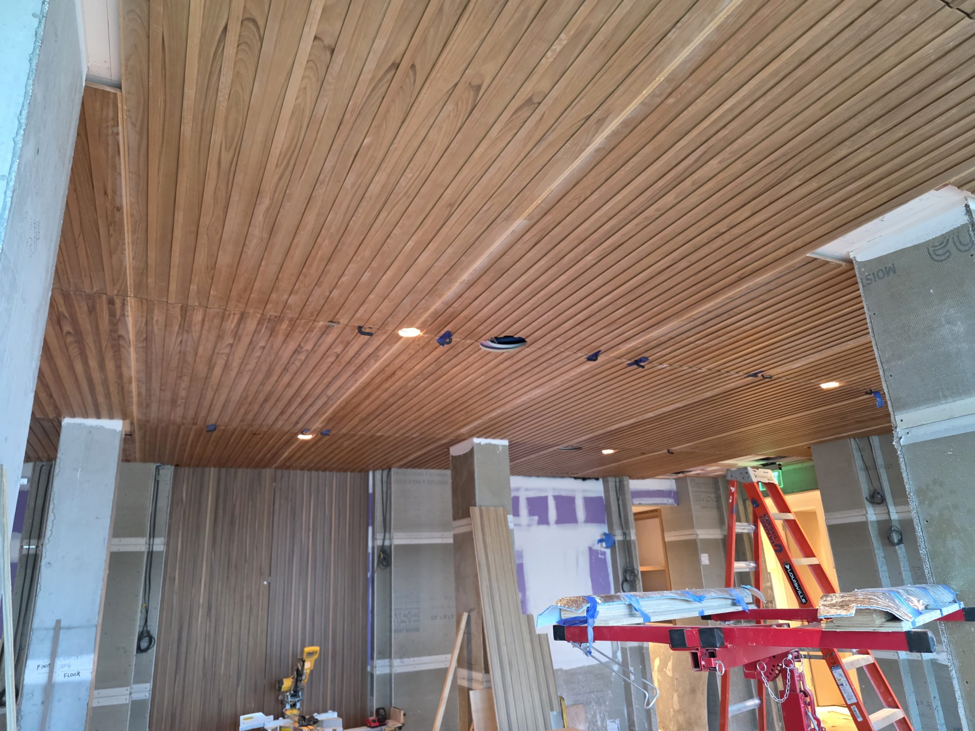 Natural tongue-and-groove linear wood plank ceiling installation with integrated downlighting in progress in Winston-Salem NC