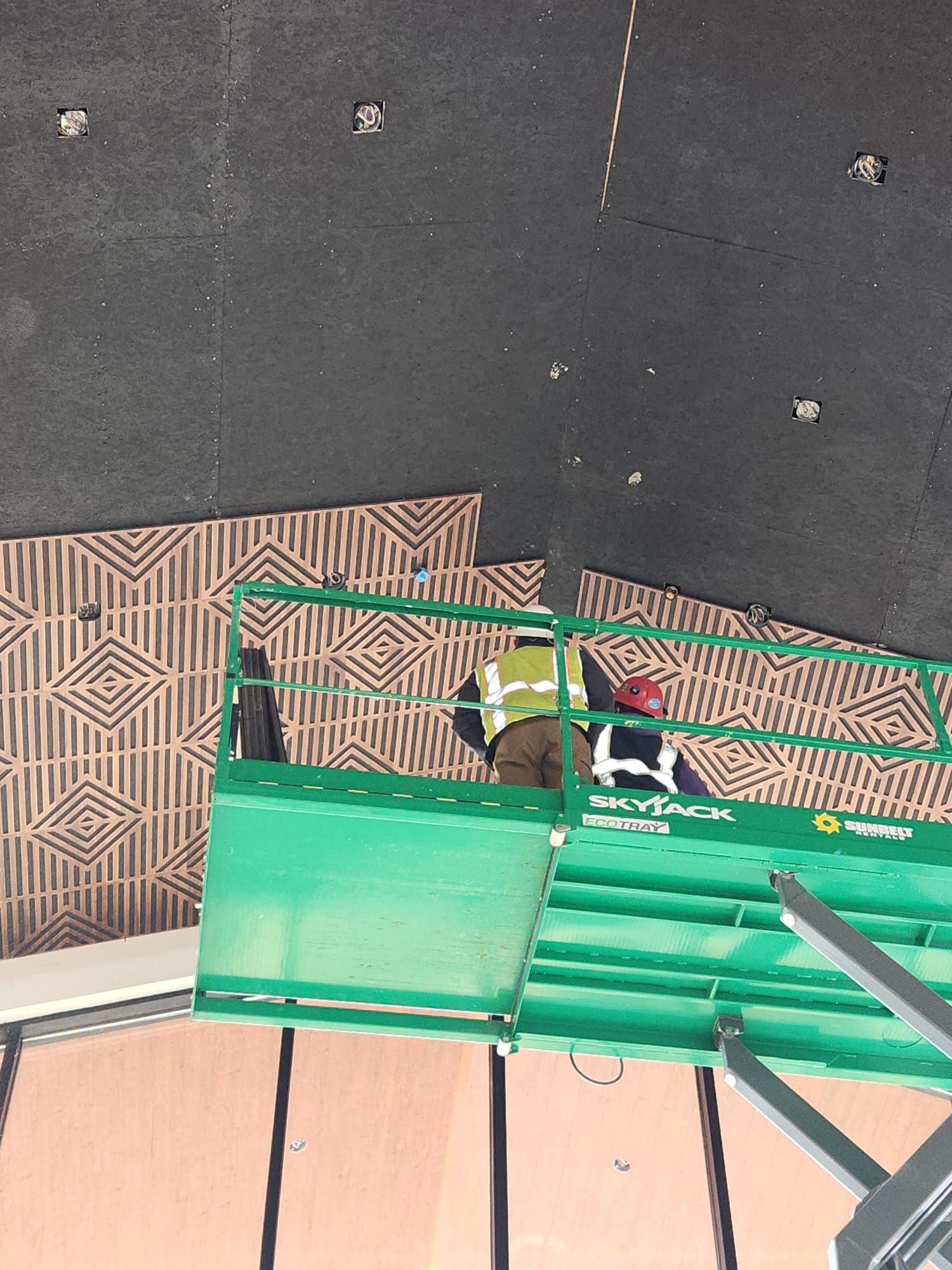 Carpenters on scissor lift installing decorative acoustic concentric diamond wood ceiling panels in Winston-Salem NC