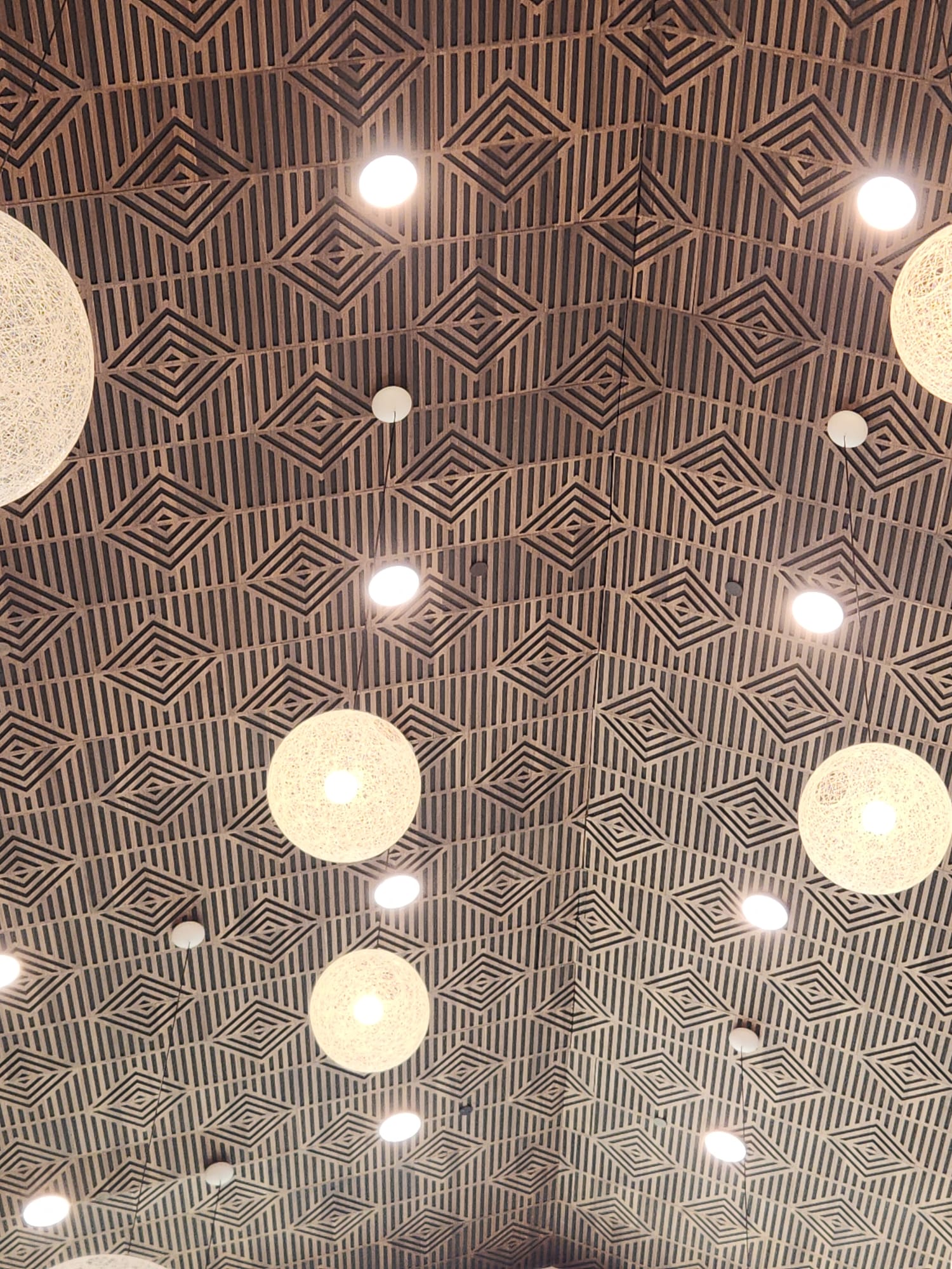 Intricate diamond geometric acoustic timber slat ceiling with suspended globe chandeliers in Greensboro NC
