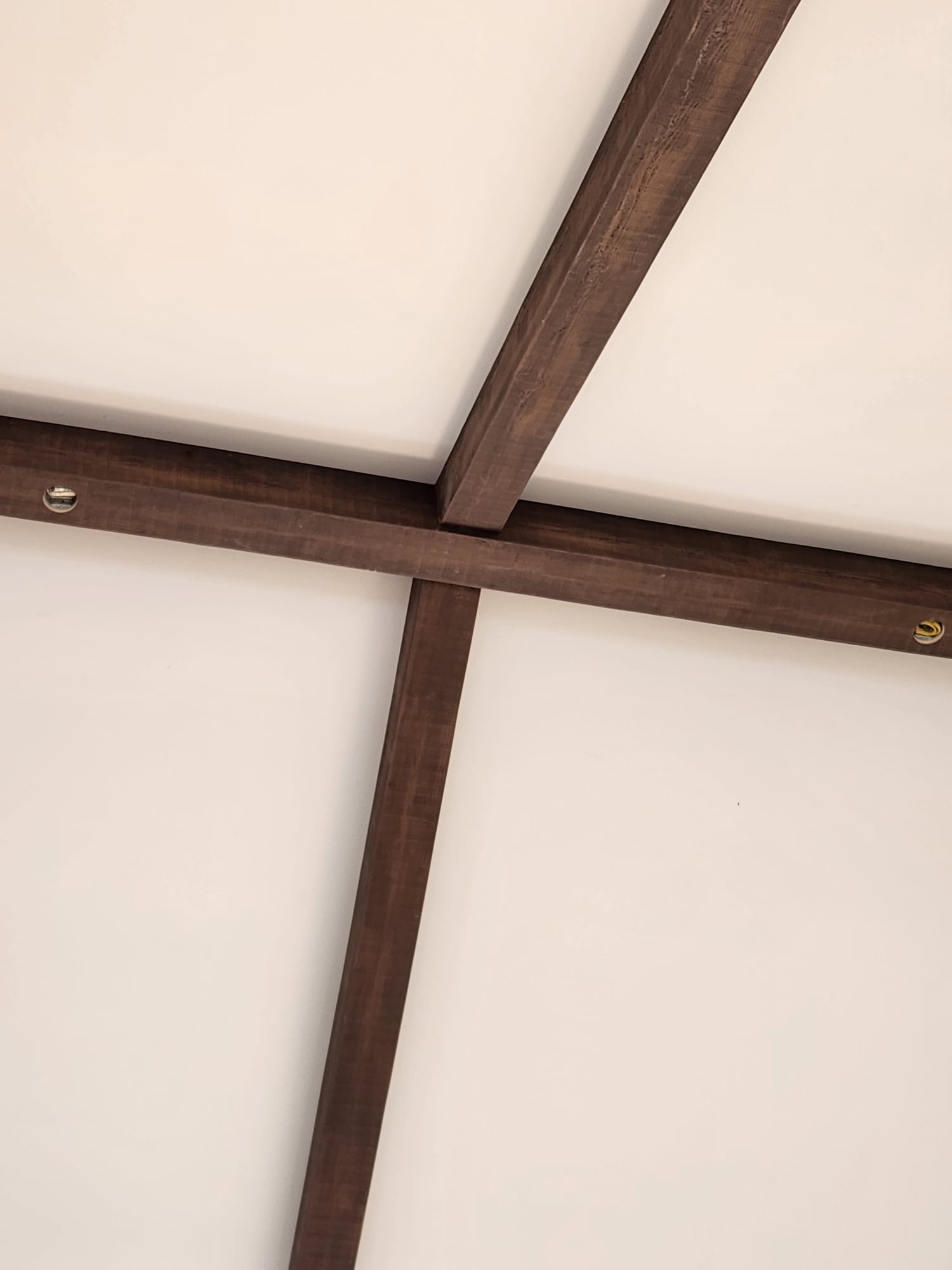 Dark stained timber ceiling beam cross-intersection installed against white ceiling in Winston-Salem NC