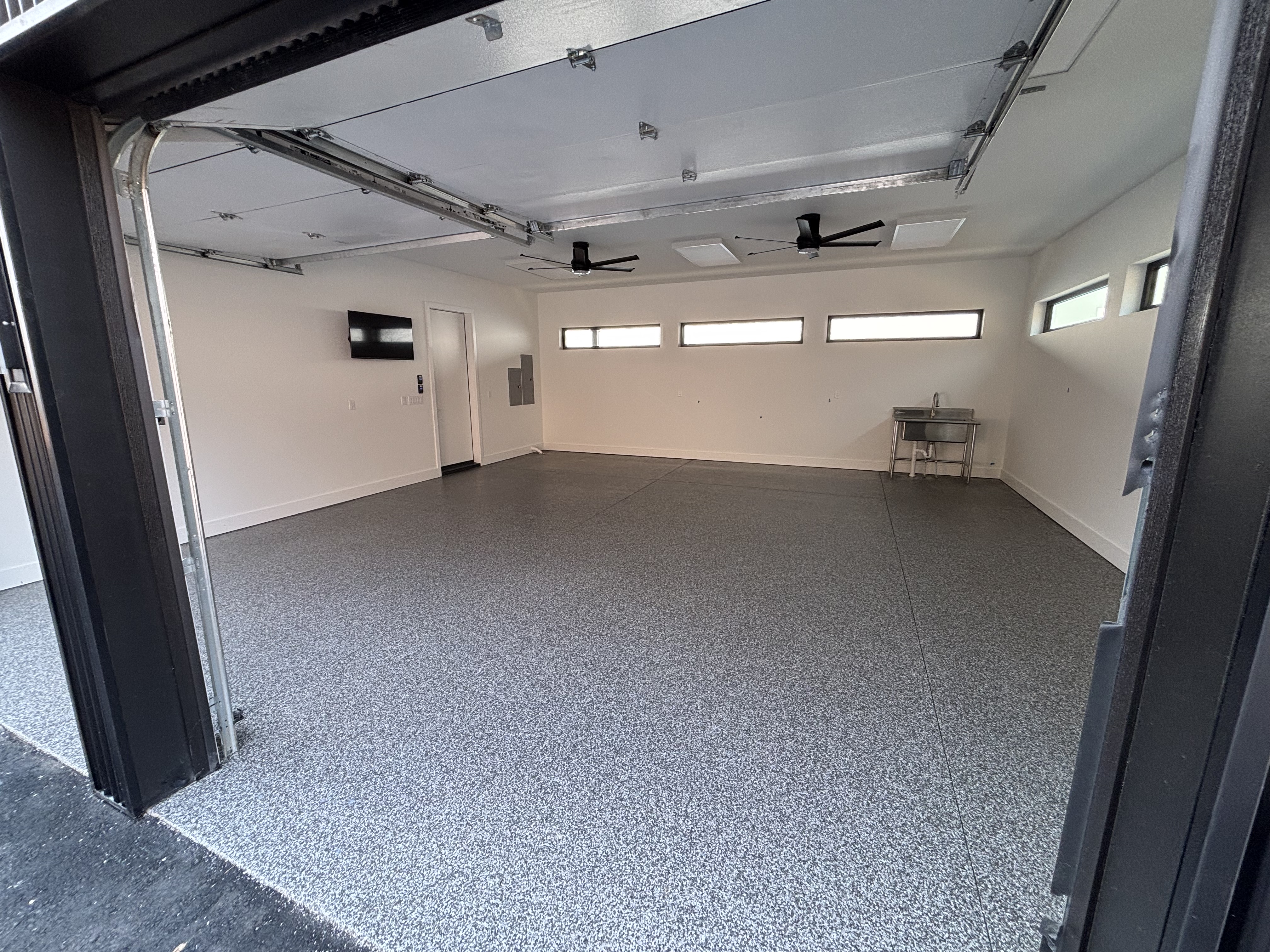 Modern luxury garage with clean gray flake floor, clerestory windows, and shop amenities