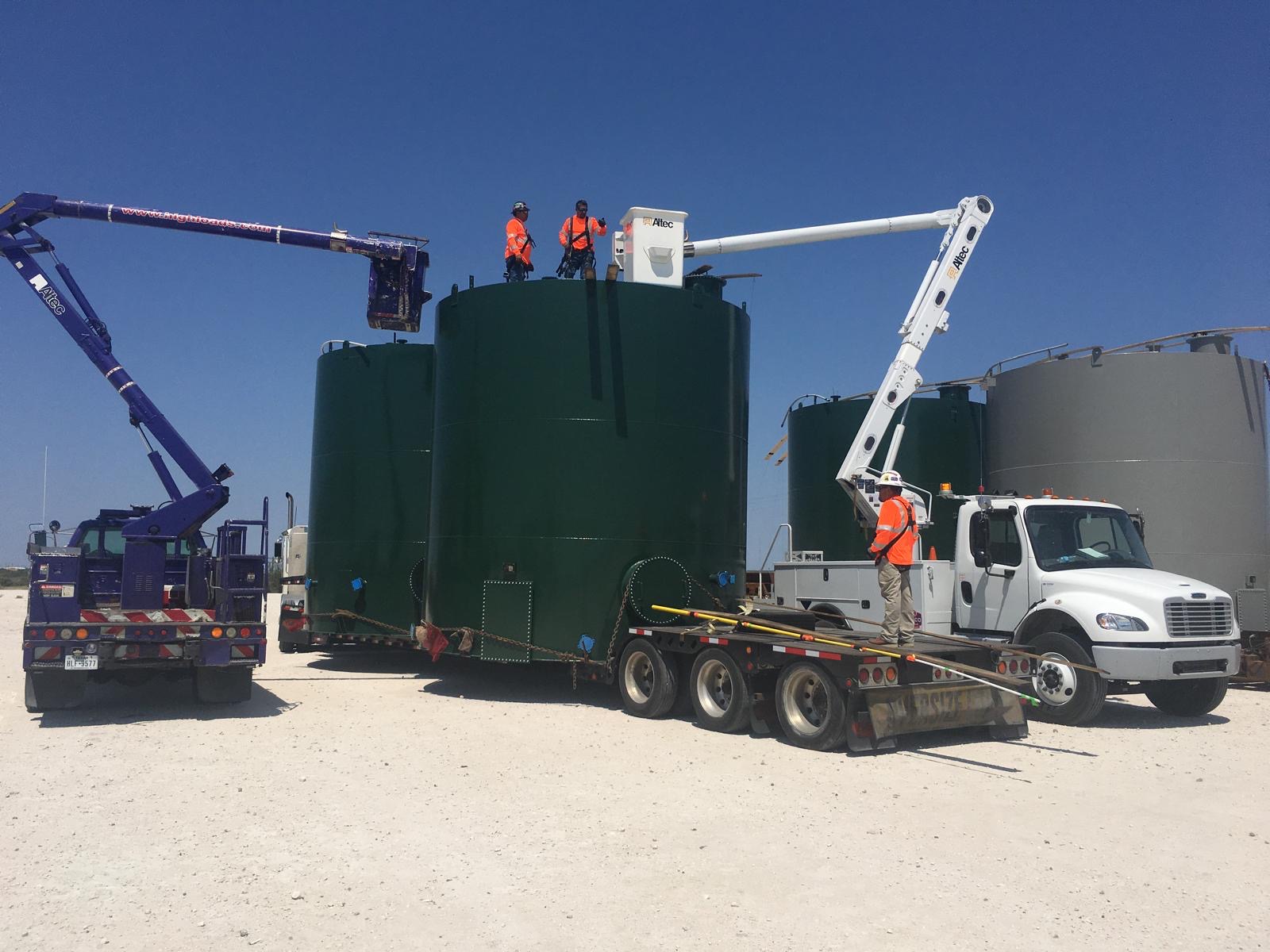 Oversized industrial storage tanks staged with bucket lift trucks coordinating clearances