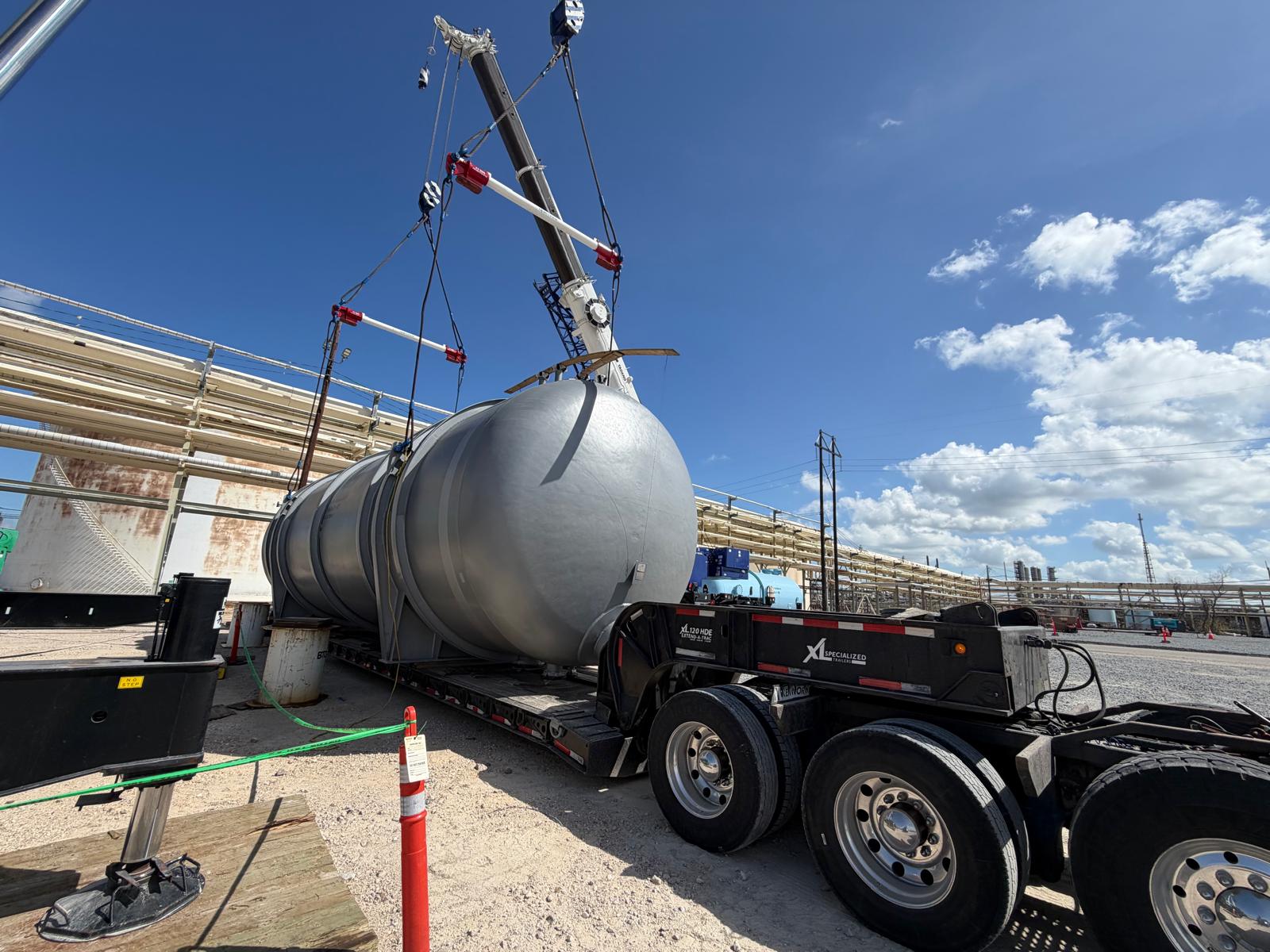 Dual crane rigging and offloading large industrial vessel from specialized trailer