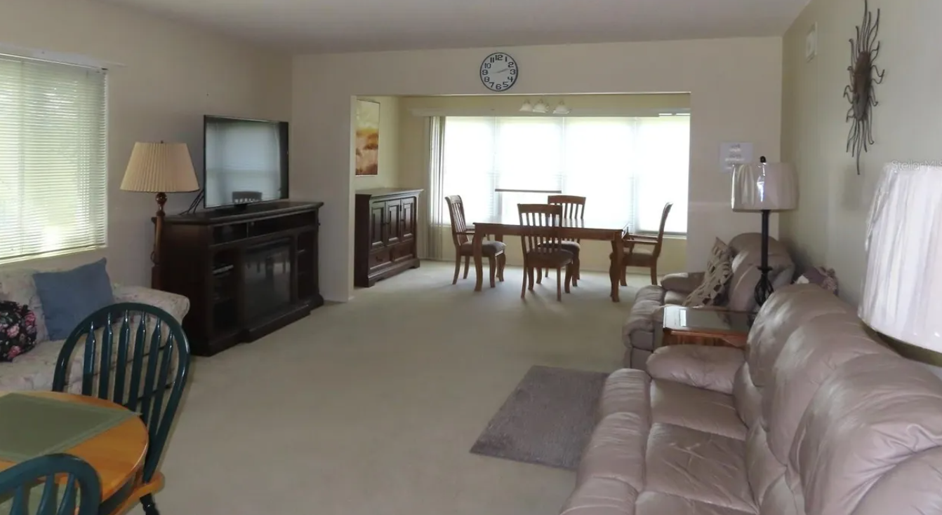 Dimly lit 1980s Florida condo living room with dated furnishings and heavy furniture before cleanout