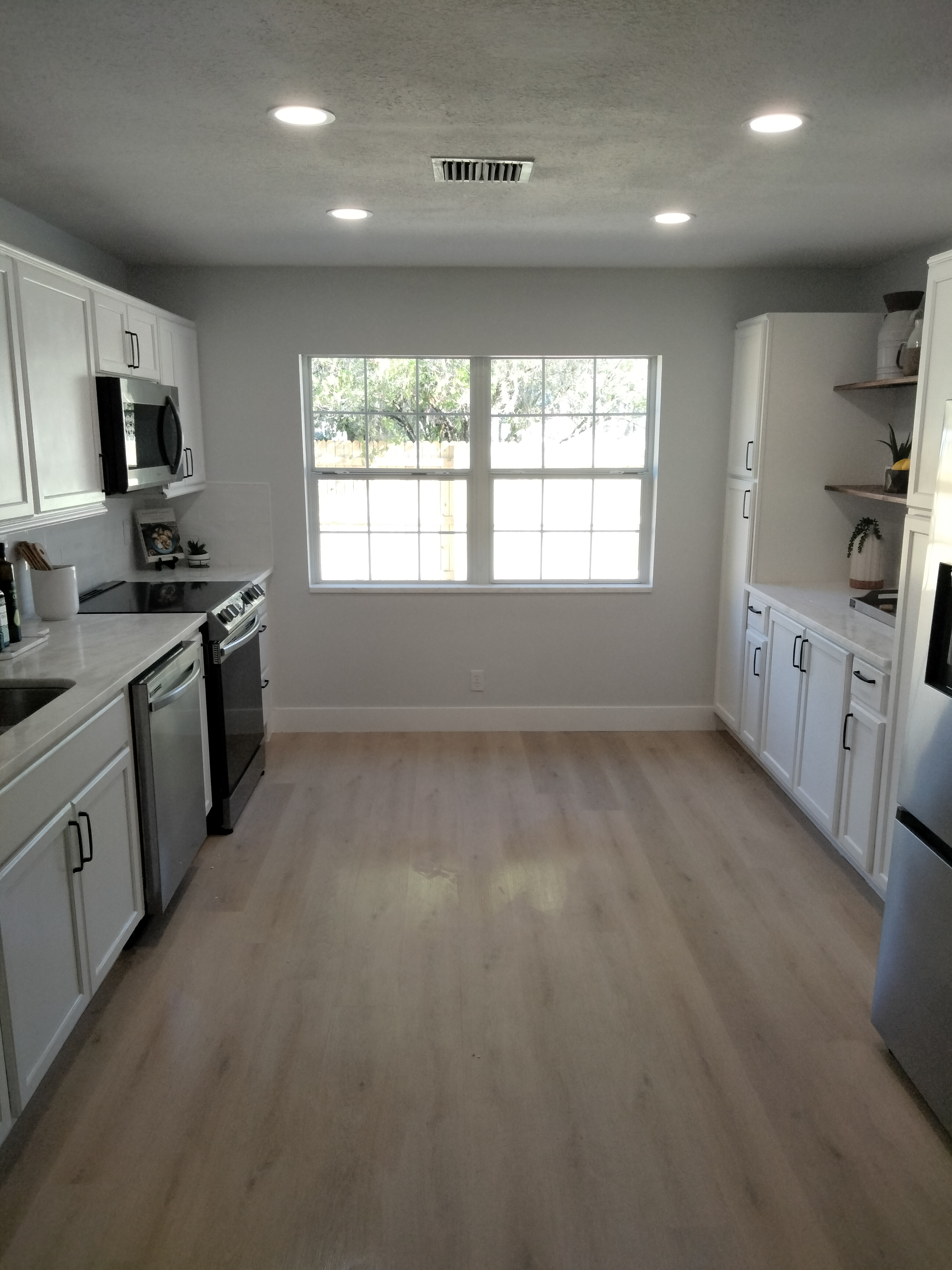 Renovated modern kitchen with white cabinetry, bright lighting, and wood-look flooring