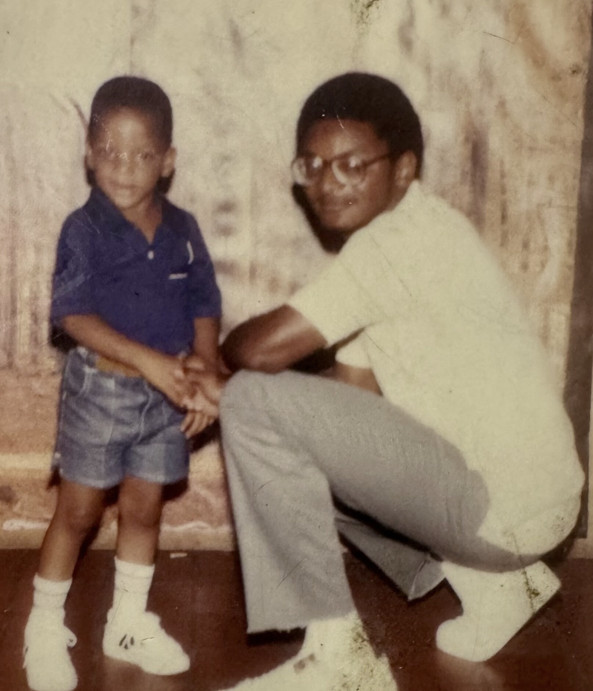 Vintage photo of young boy in blue polo shirt standing next to kneeling man in white outfit