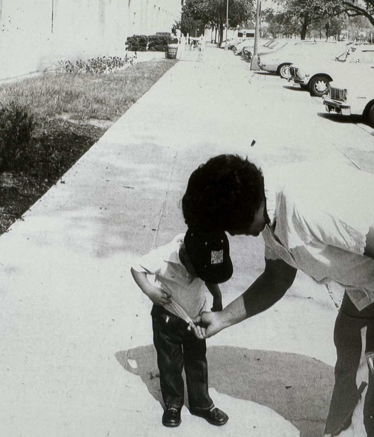 Black and white photograph of an adult helping a small child on a city sidewalk