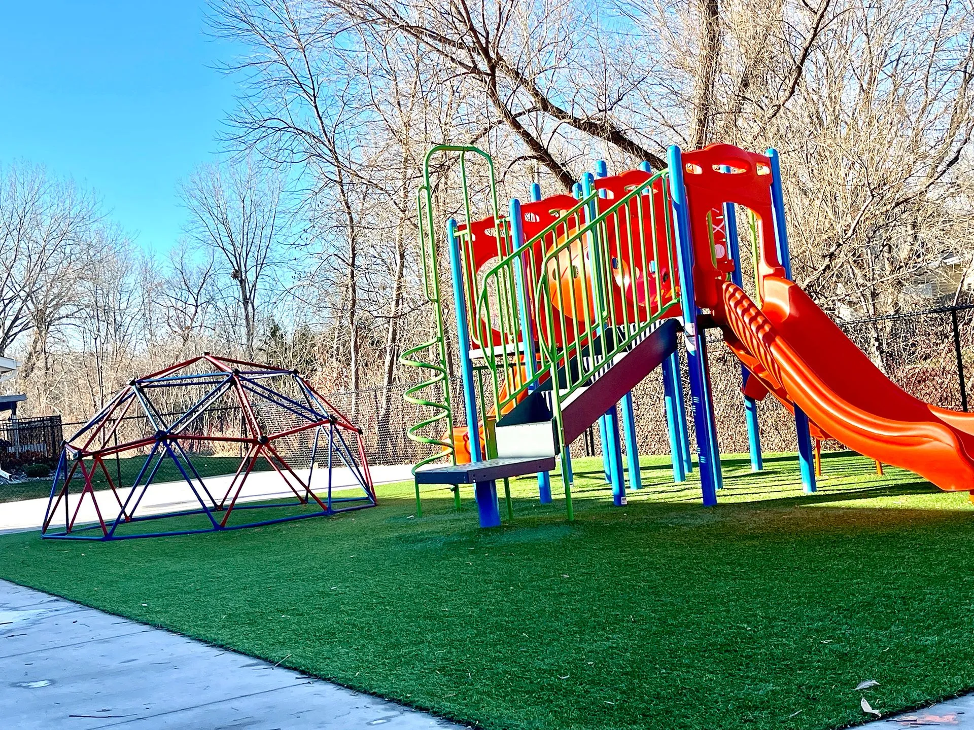 Outdoor playground with slide play structure and geodesic climbing dome on turf