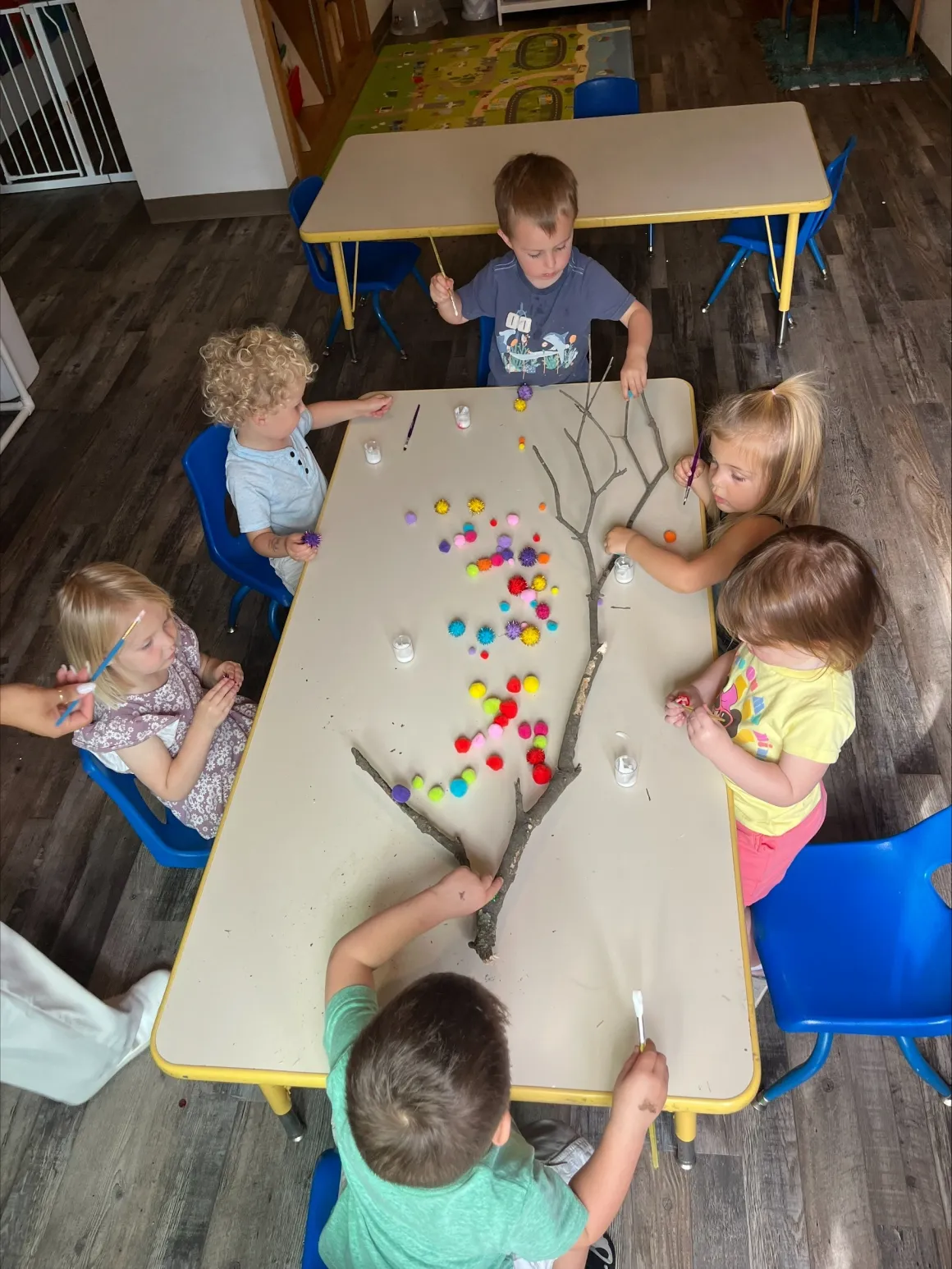Collaborative nature tree branch art project with pom-poms and paint brushes