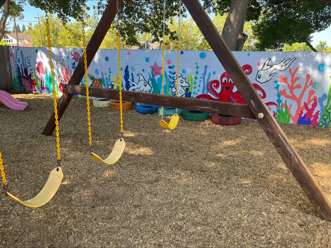 Outdoor swing set with colorful ocean mural wall and shaded play yard