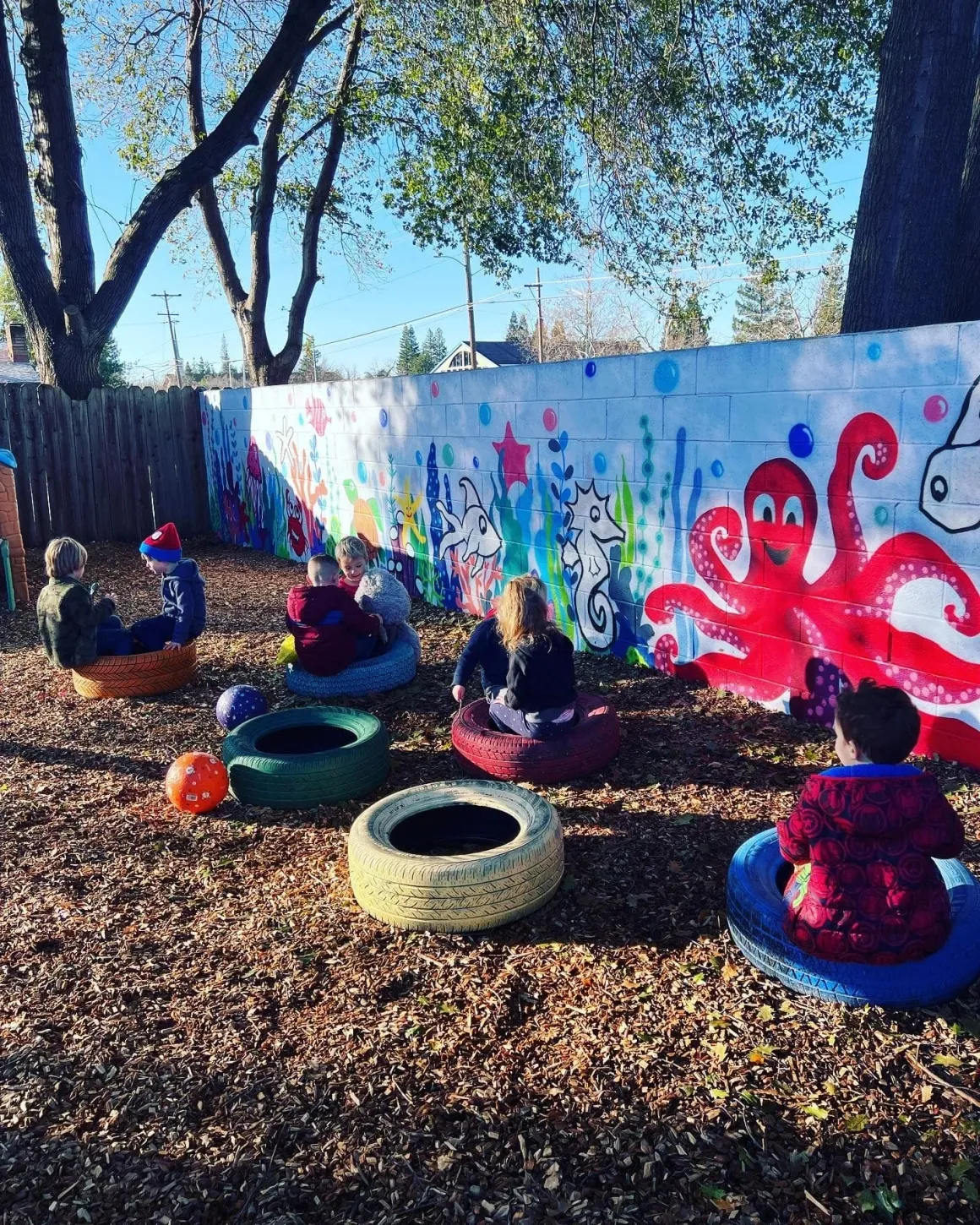 Outdoor playground circle time seating on colorful painted tires along the sea life mural