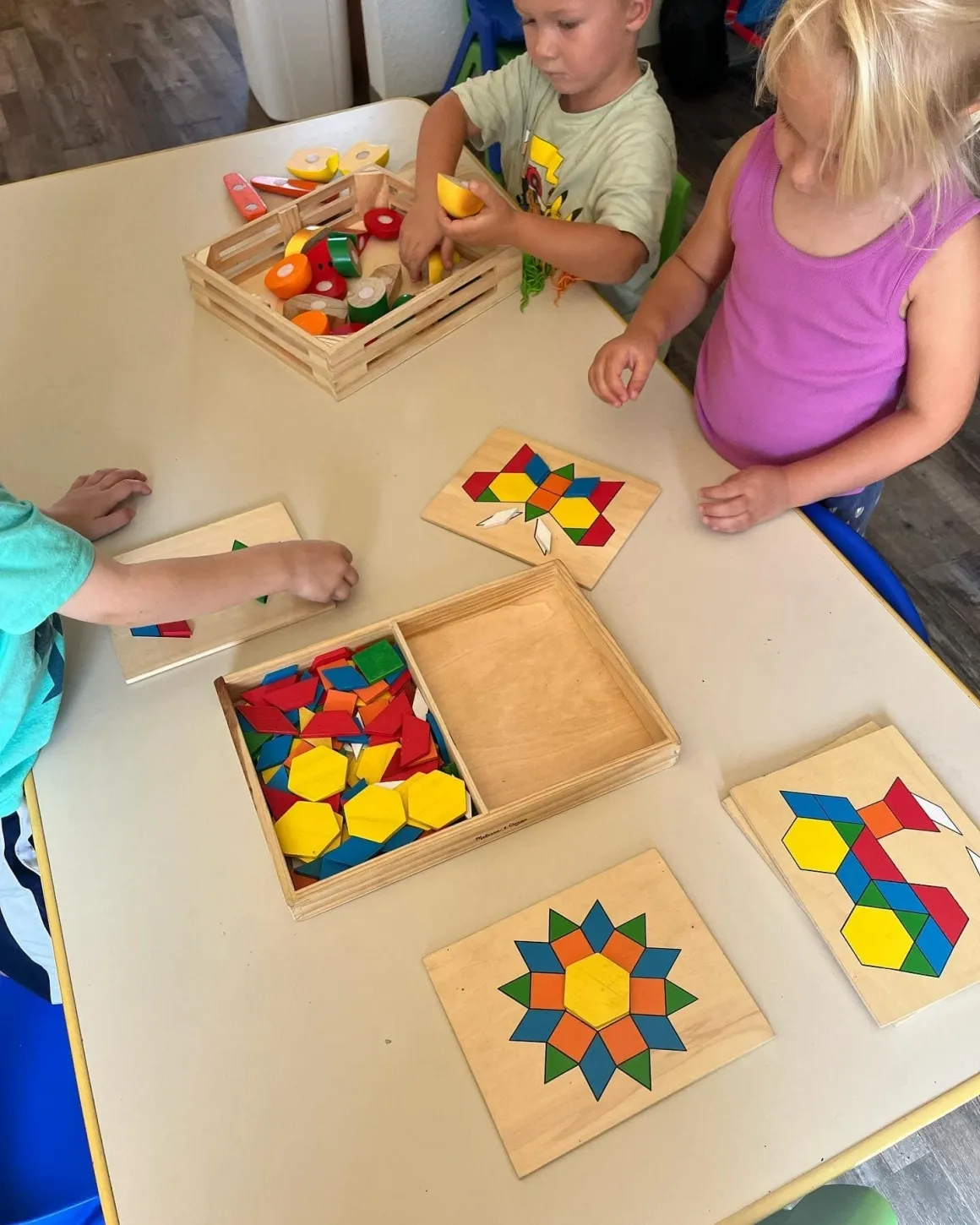 Preschoolers exploring geometric tangram and wooden pattern block puzzles at the activity table