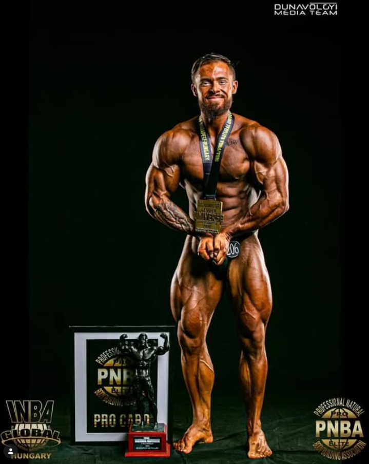 James Alabaster holding INBA / PNBA Pro Card award and medal on stage