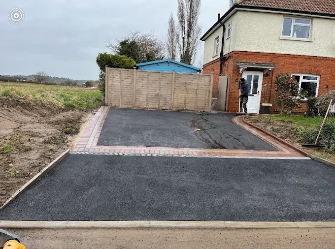 Smooth rolled black tarmac driveway with multi-tone block paved borders and integrated channel drain