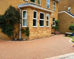 Sweeping resin-bound driveway with curved block-paved borders outside brick home