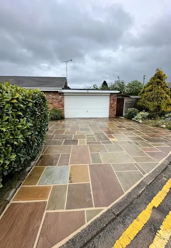 Multi-tonal natural stone flagstone driveway leading to garage and mature hedge