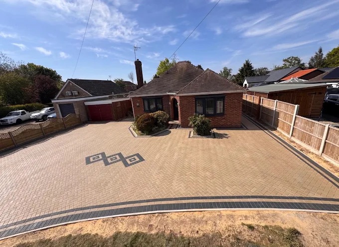 Large front block paved driveway with geometric diamond motifs and curved charcoal border course