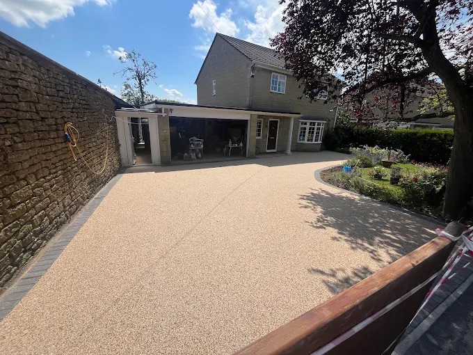 Spacious resin-bound front driveway with dark block-paved border along Cotswold stone wall
