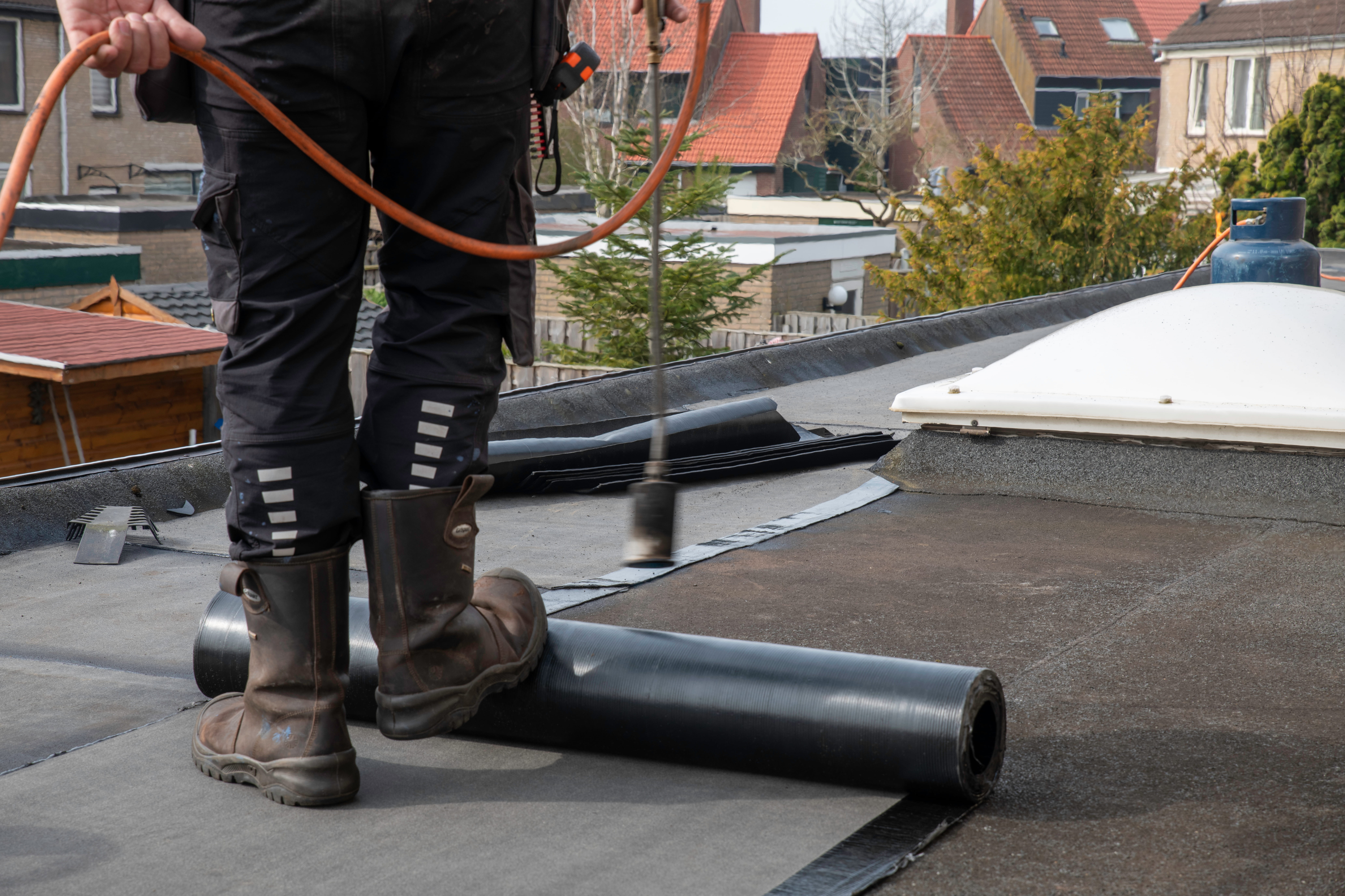 Roofer applying torch-on felt waterproofing membrane on residential flat roof