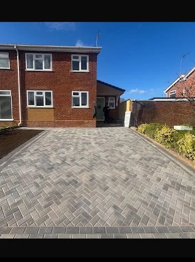 Silver-grey herringbone block paving driveway with charcoal border course outside red brick home