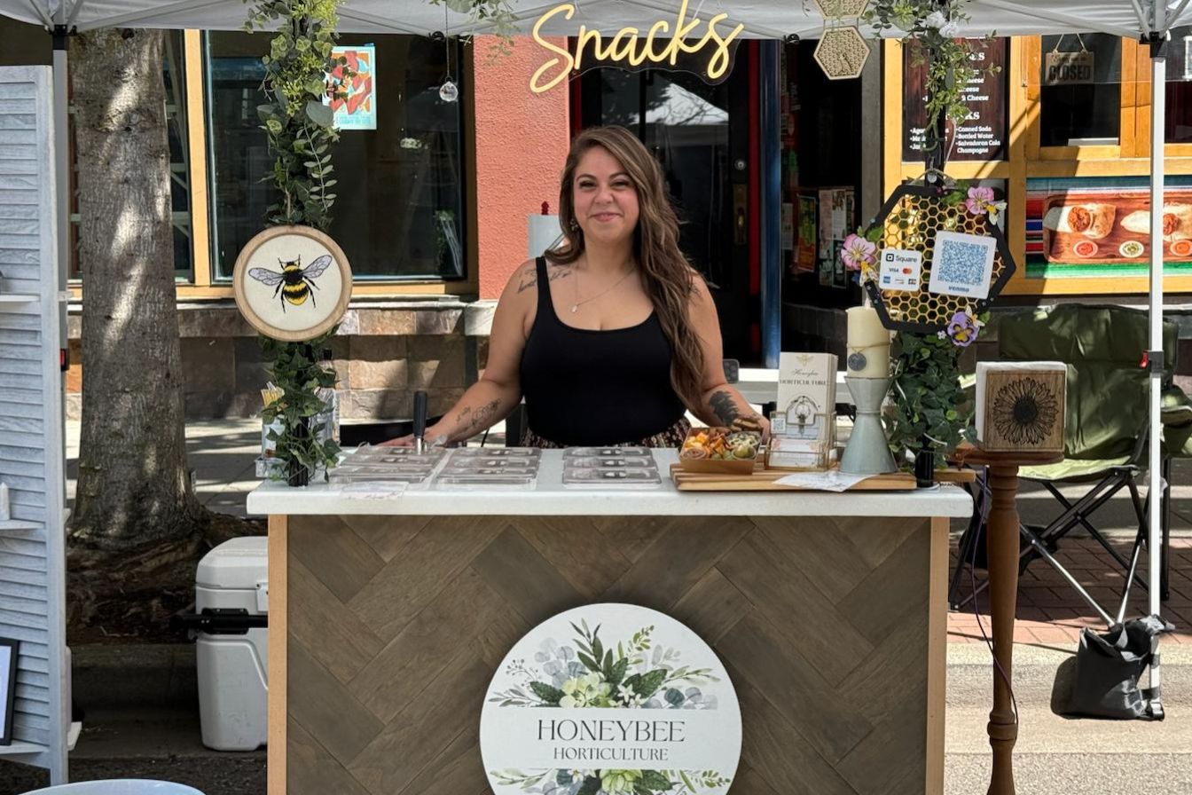 Honeybee Horticulture founder at mobile charcuterie cart booth with bumble bee logo and grazing station display