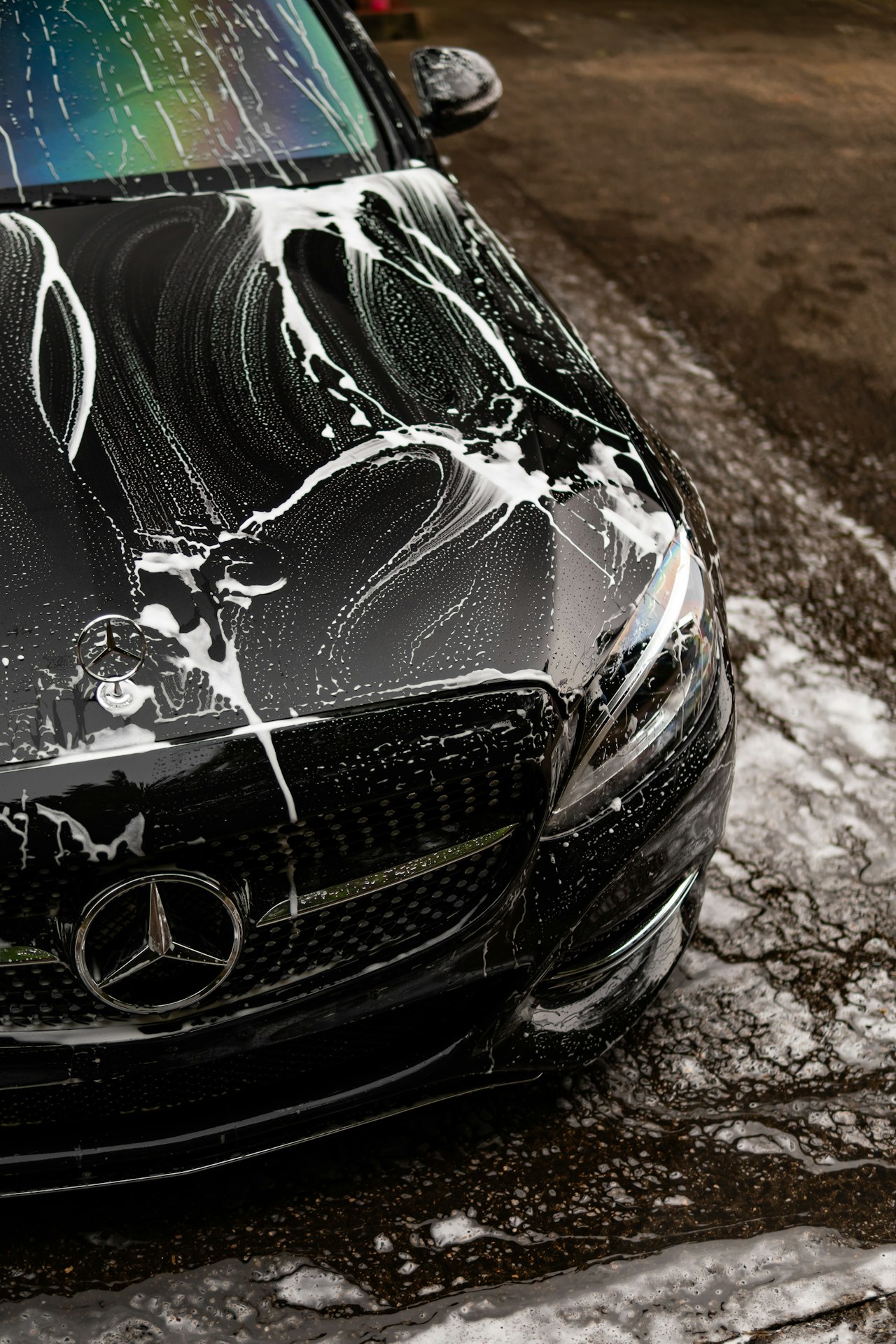 Black luxury car covered in thick soap foam during a professional hand wash