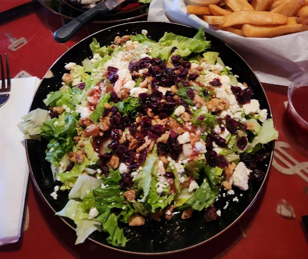 Wildhorse Bar & Grill fresh Cranberry Walnut Salad on a black plate with crisp greens, candied walnuts, dried cranberries, and crumbled feta cheese with raspberry vinaigrette