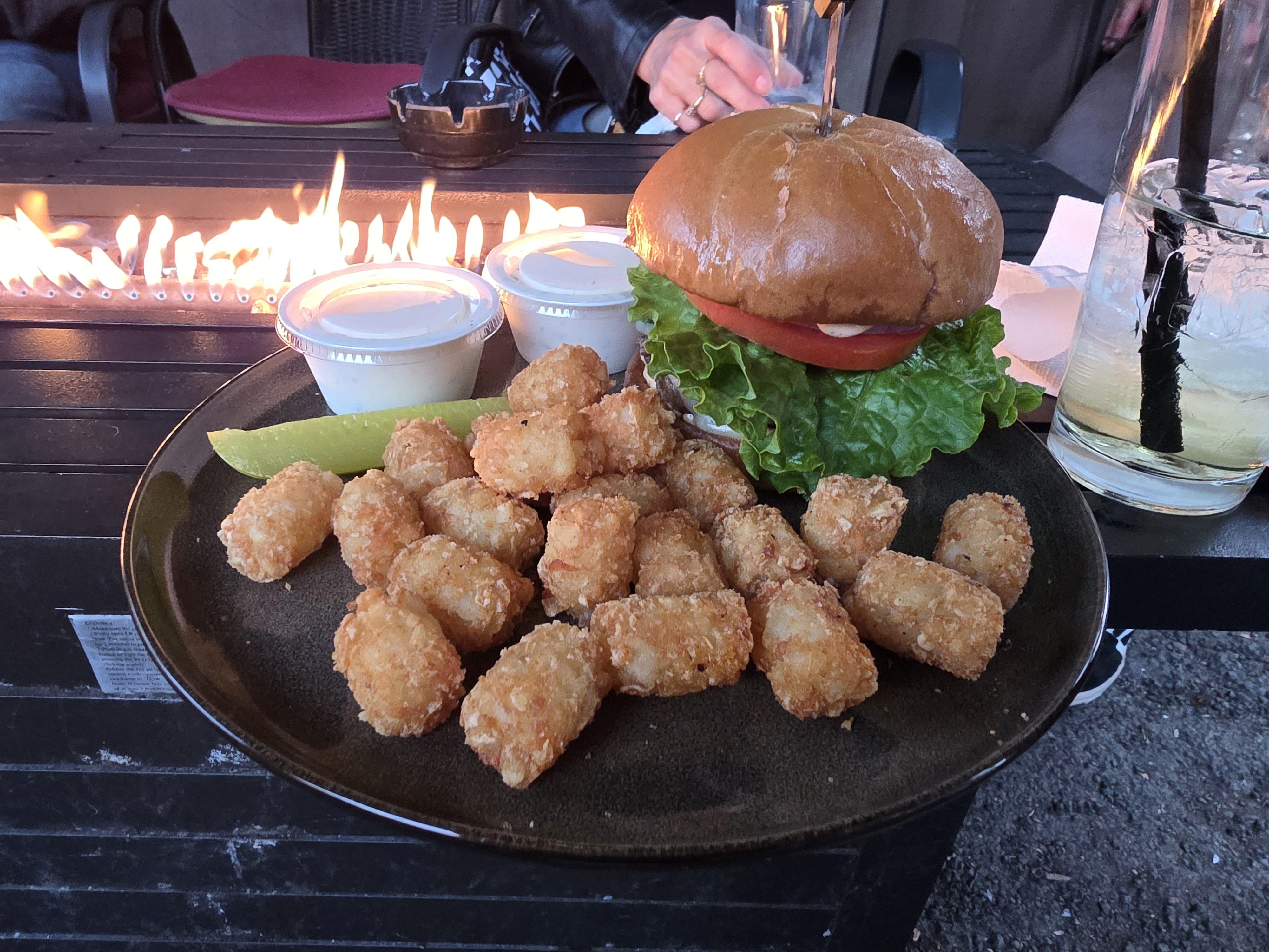 Wildhorse Bar & Grill fresh hand-pressed burger on a pub bun with crispy tater tots, dill pickle spear, and dipping sauces by the fire table