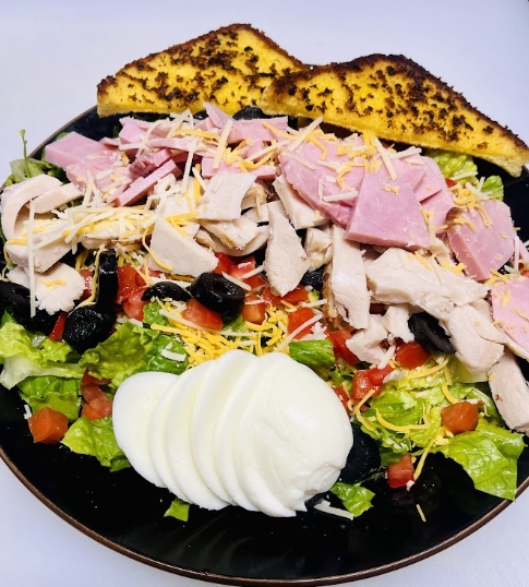 Wildhorse Bar & Grill Chef Salad loaded with sliced turkey, ham, shredded cheese, olives, tomatoes, sliced hard-boiled egg, and toasted garlic bread
