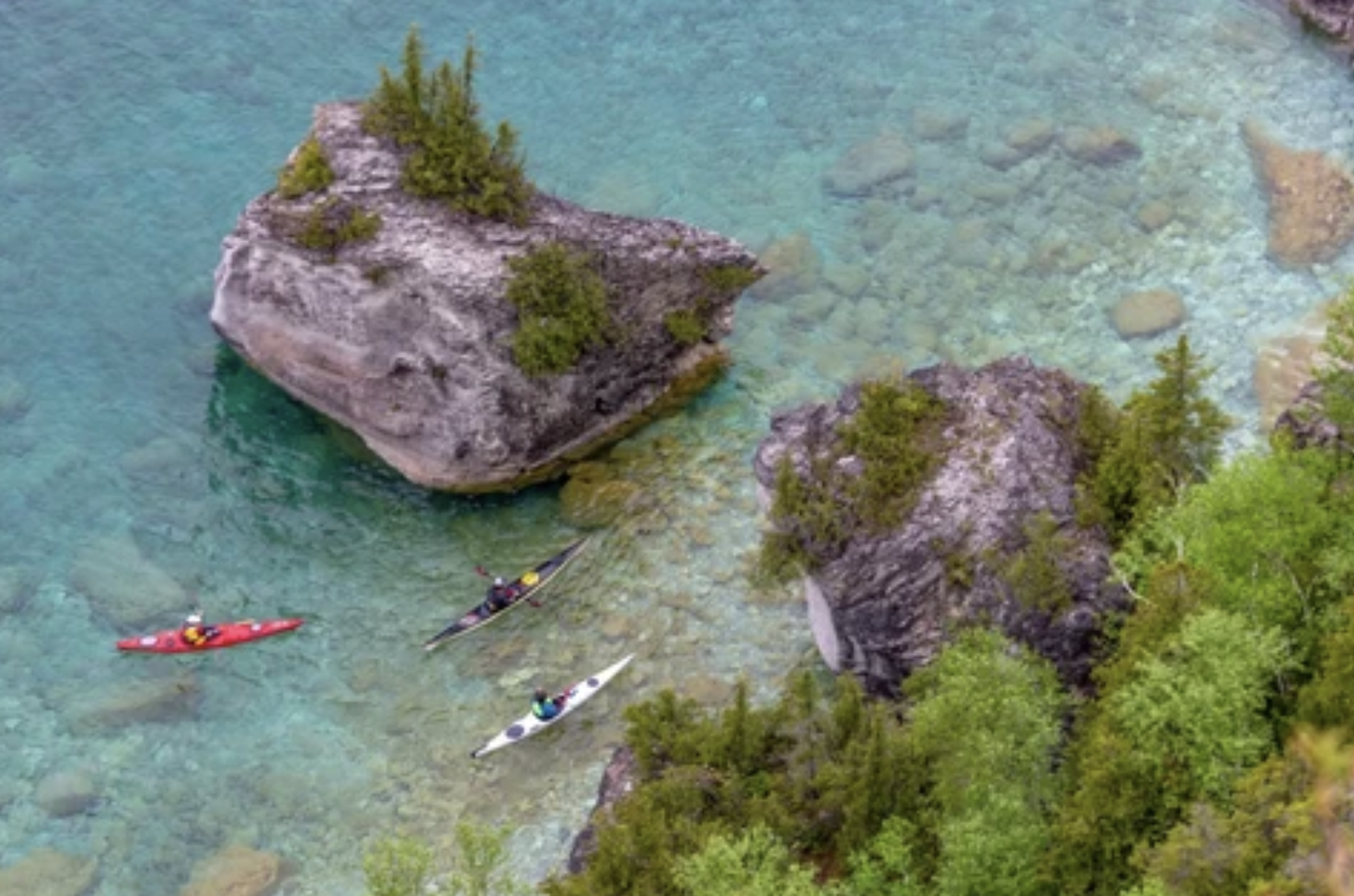 Kayakers paddling through turquoise shallows around limestone boulders on Georgian Bay