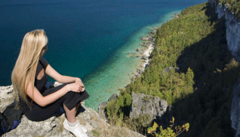 Hiker sitting atop the Niagara Escarpment cliffs along the Bruce Trail overlooking turquoise Georgian Bay