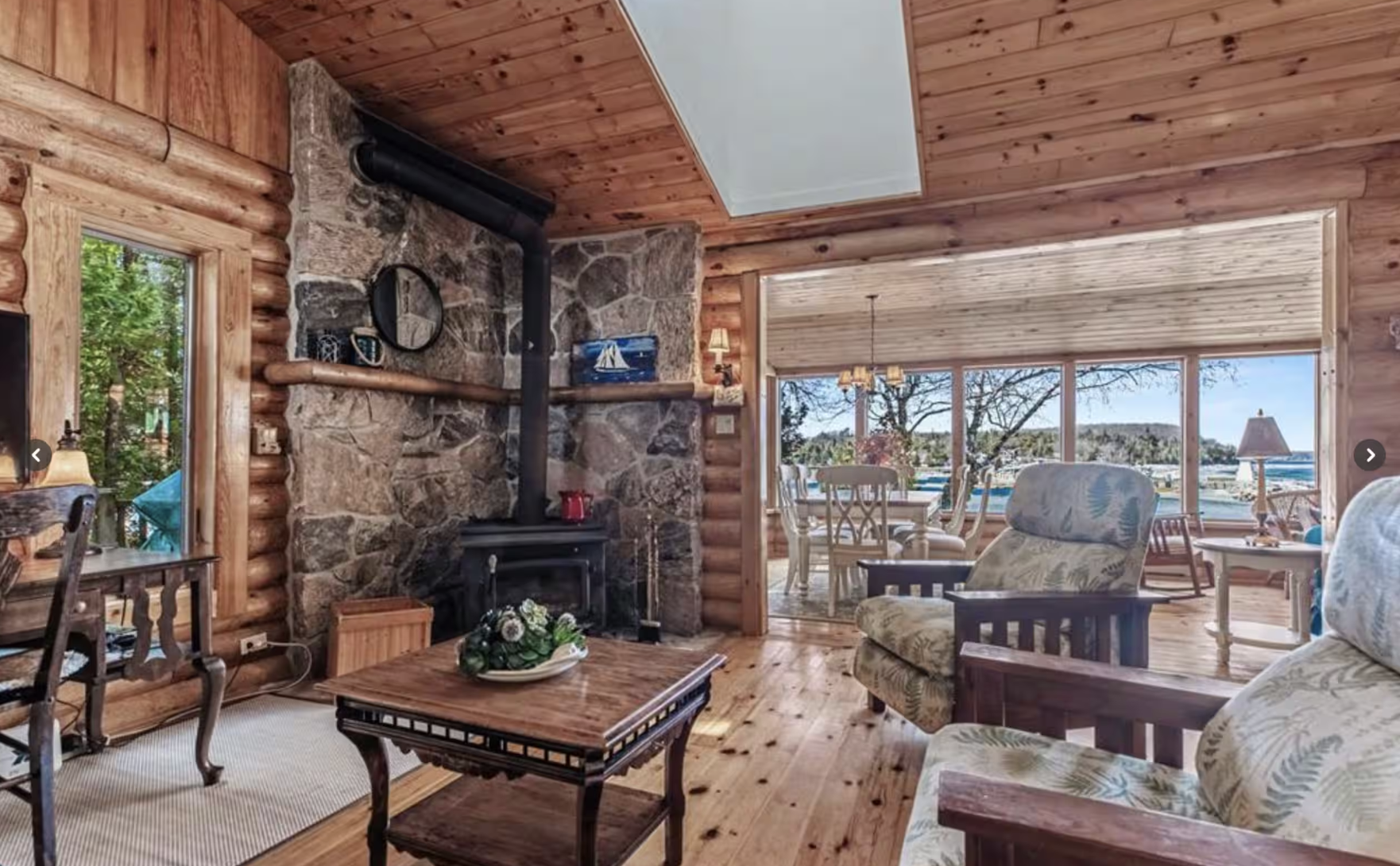Lodge living room with stone wood stove fireplace, pine floors, and sunroom dining view