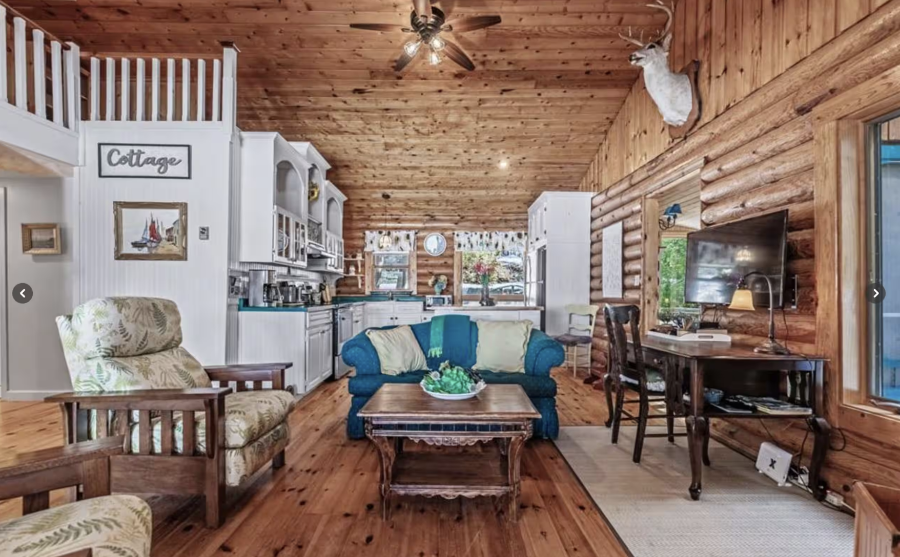 Great room sitting area and kitchen with handcrafted log walls and high wood ceiling