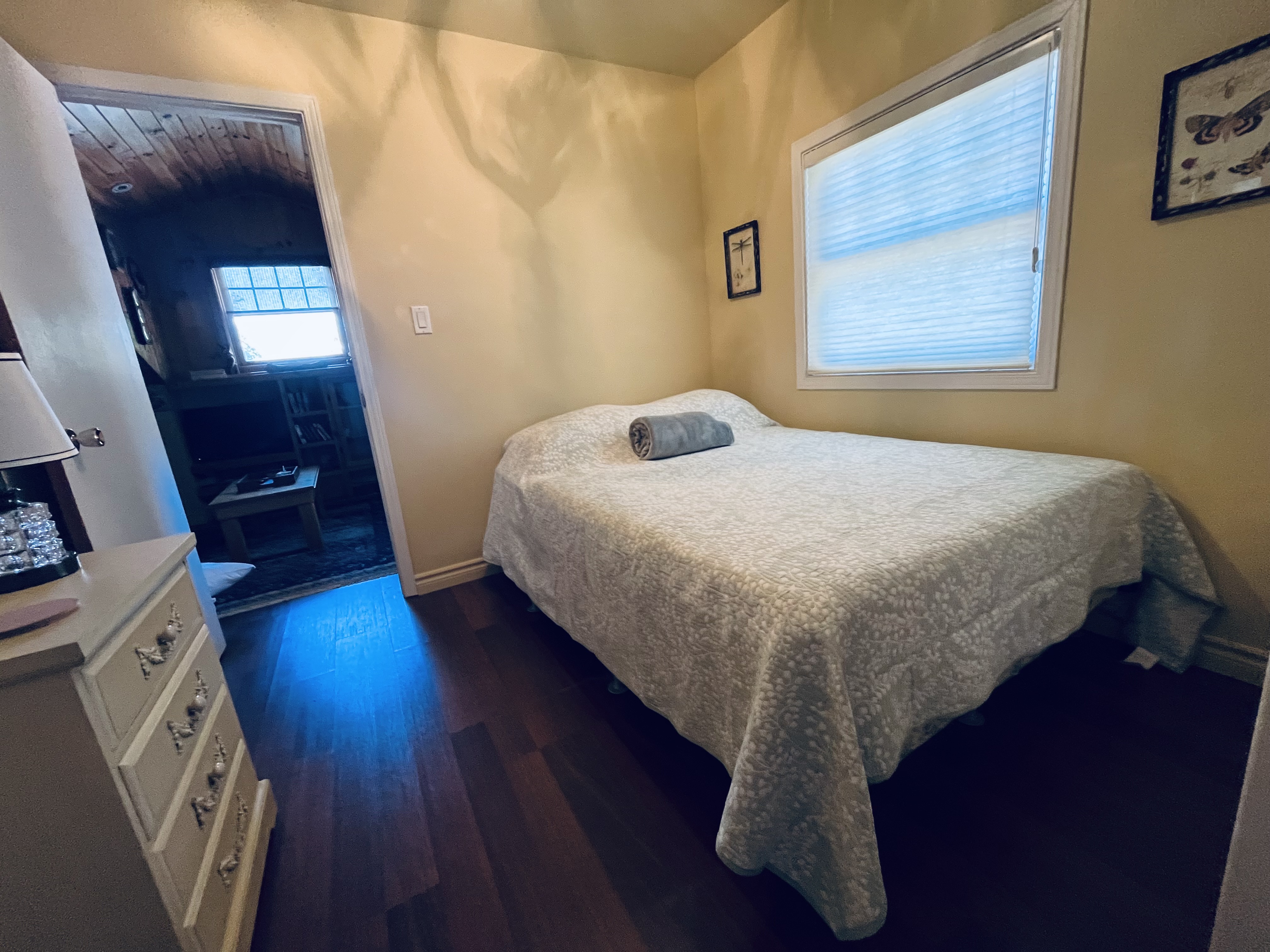 Bright and serene guest bedroom with soft linens, dresser, and natural window light