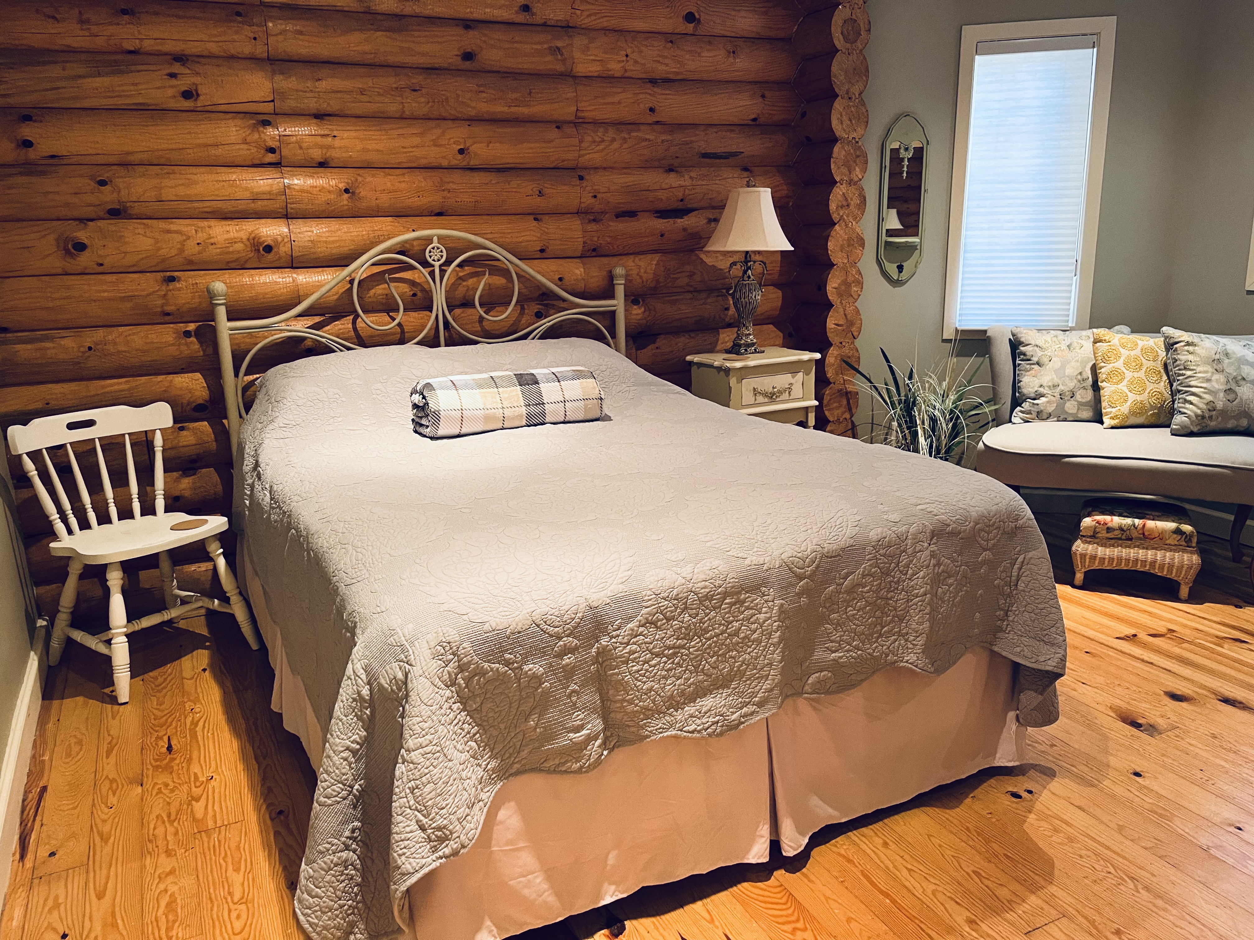 Primary log lodge bedroom with iron bed, plush quilt, nightstand, and reading nook