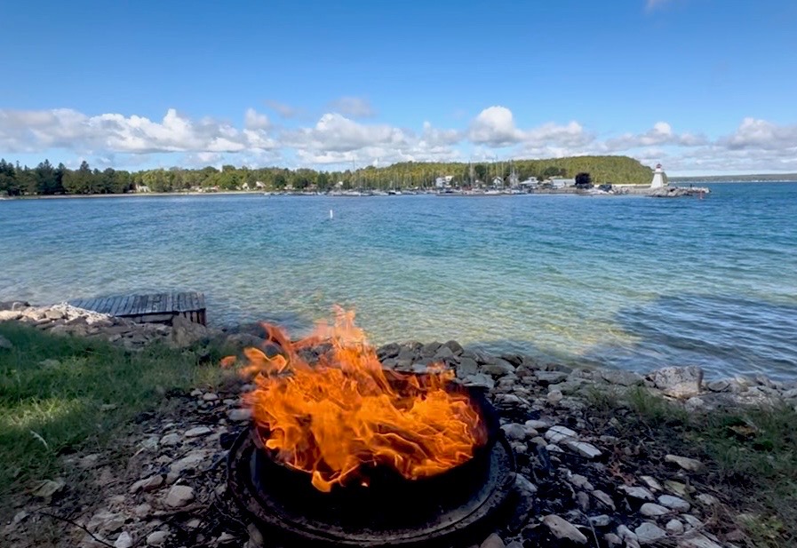 Campfire by the shore with crystal-clear turquoise waters and Lion's Head lighthouse