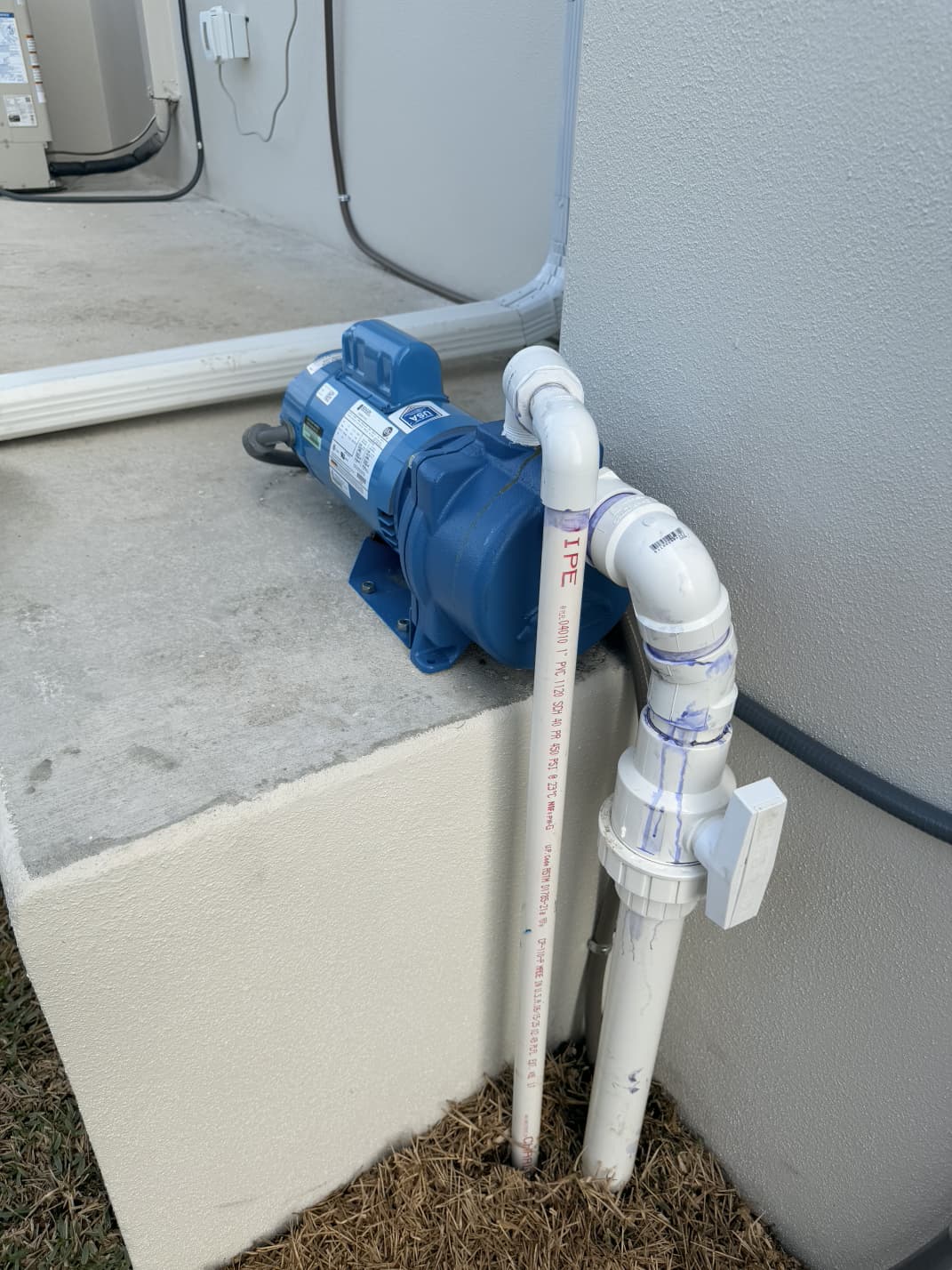 blue booster pump on concrete foundation with PVC pipe fittings and shut-off ball valve