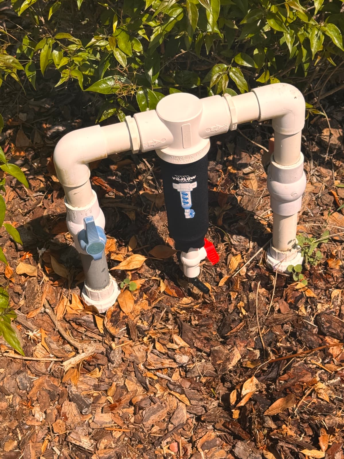 Vu-Flow spin-down sediment filter with PVC shut-off valves in landscape mulch bed by Aenlle Home Service LLC