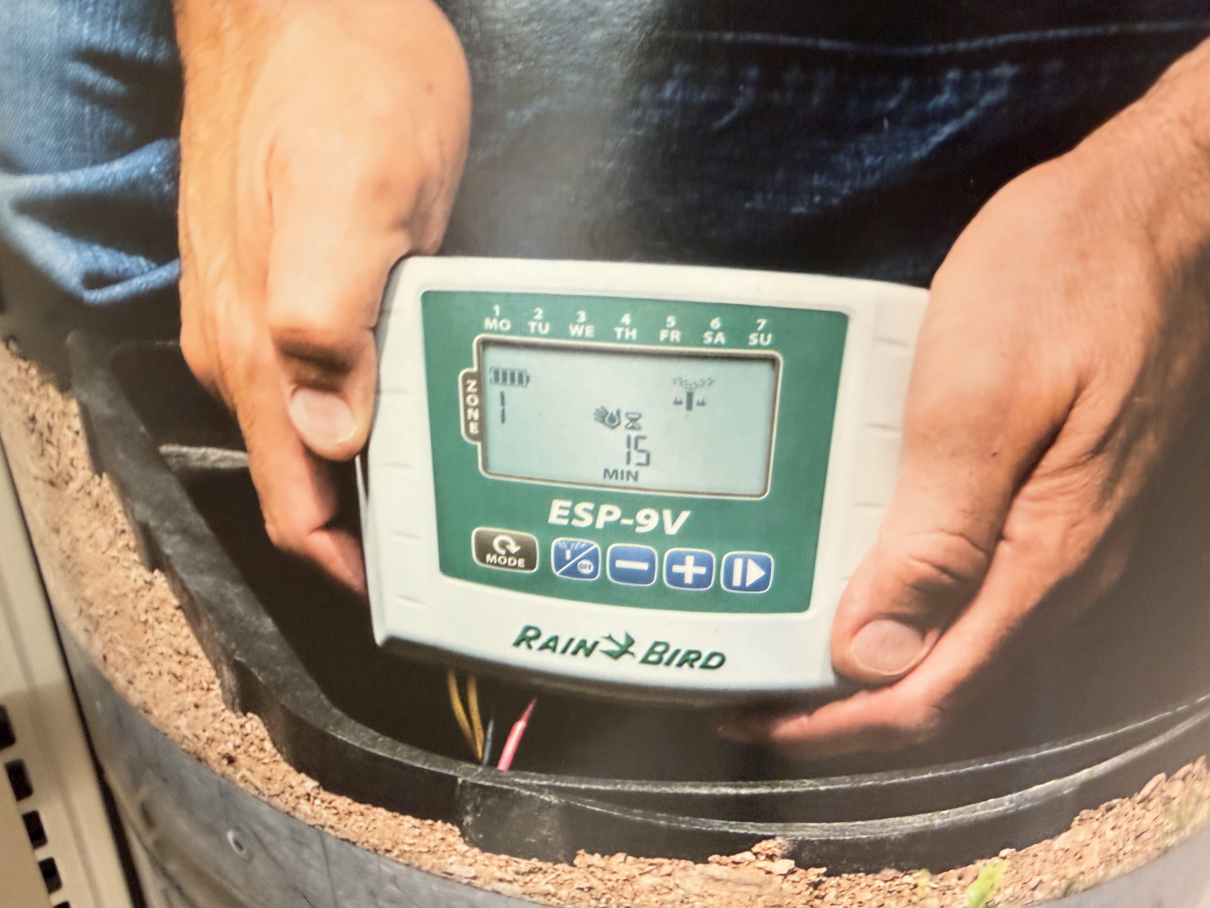 technician configuring Rain Bird ESP-9V battery-operated irrigation controller in in-ground valve box