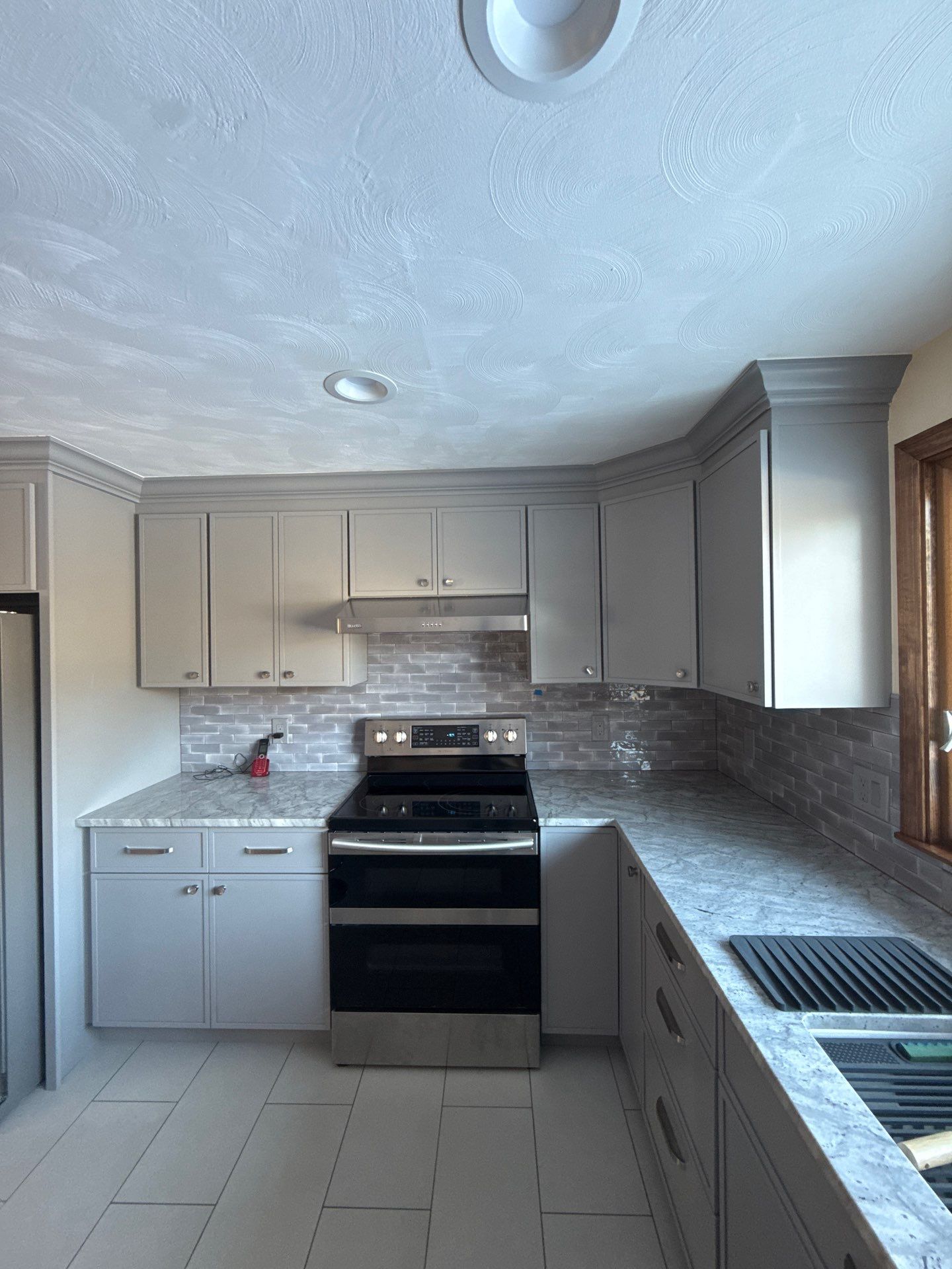 Completed kitchen remodel with soft grey shaker cabinets, quartz countertops, and glossy tile backsplash