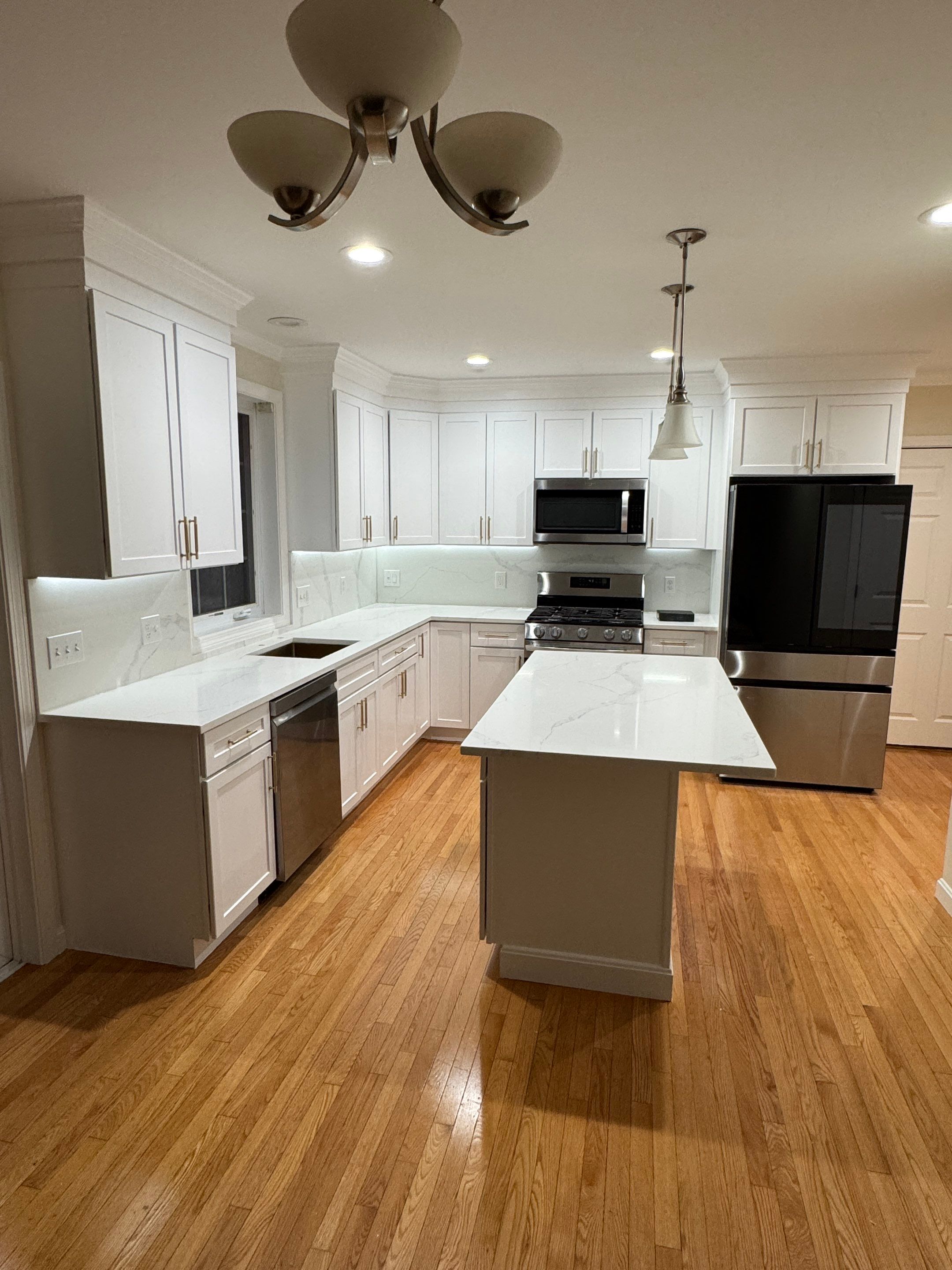 Completed bright white kitchen remodel with freestanding quartz island, warm oak floors, and gold cabinet hardware