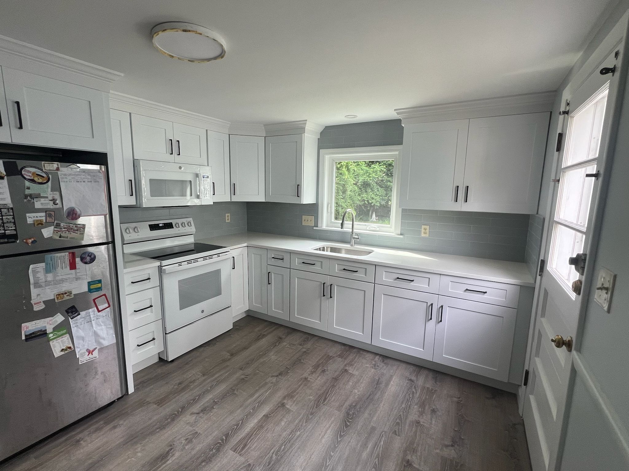 After remodel: clean white shaker cabinets, quartz countertops, subway tile backsplash, matte black hardware, and luxury plank floors