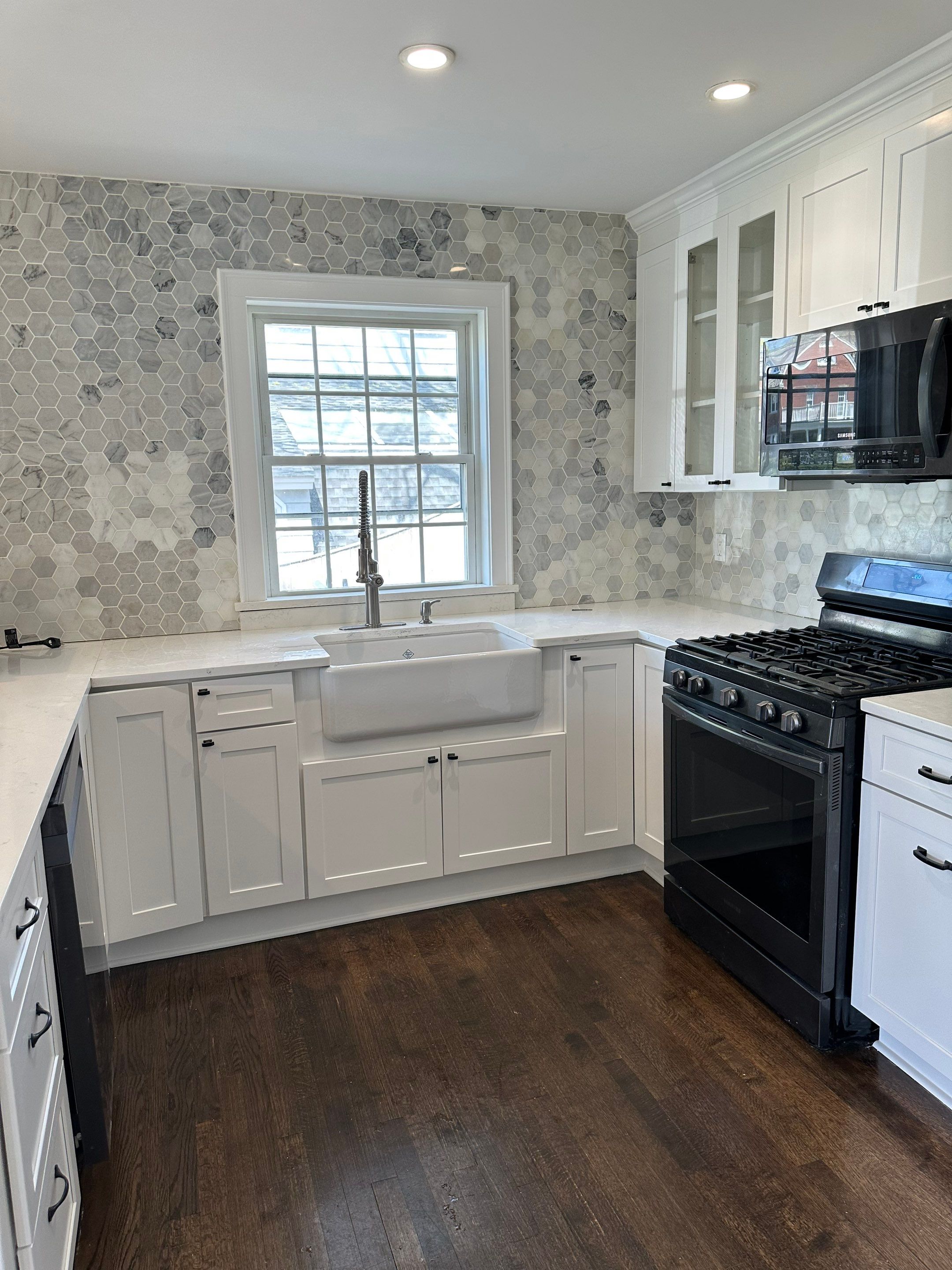 Completed crisp white painted kitchen cabinets with marble hexagon backsplash, apron front sink, and dark hardwood floors