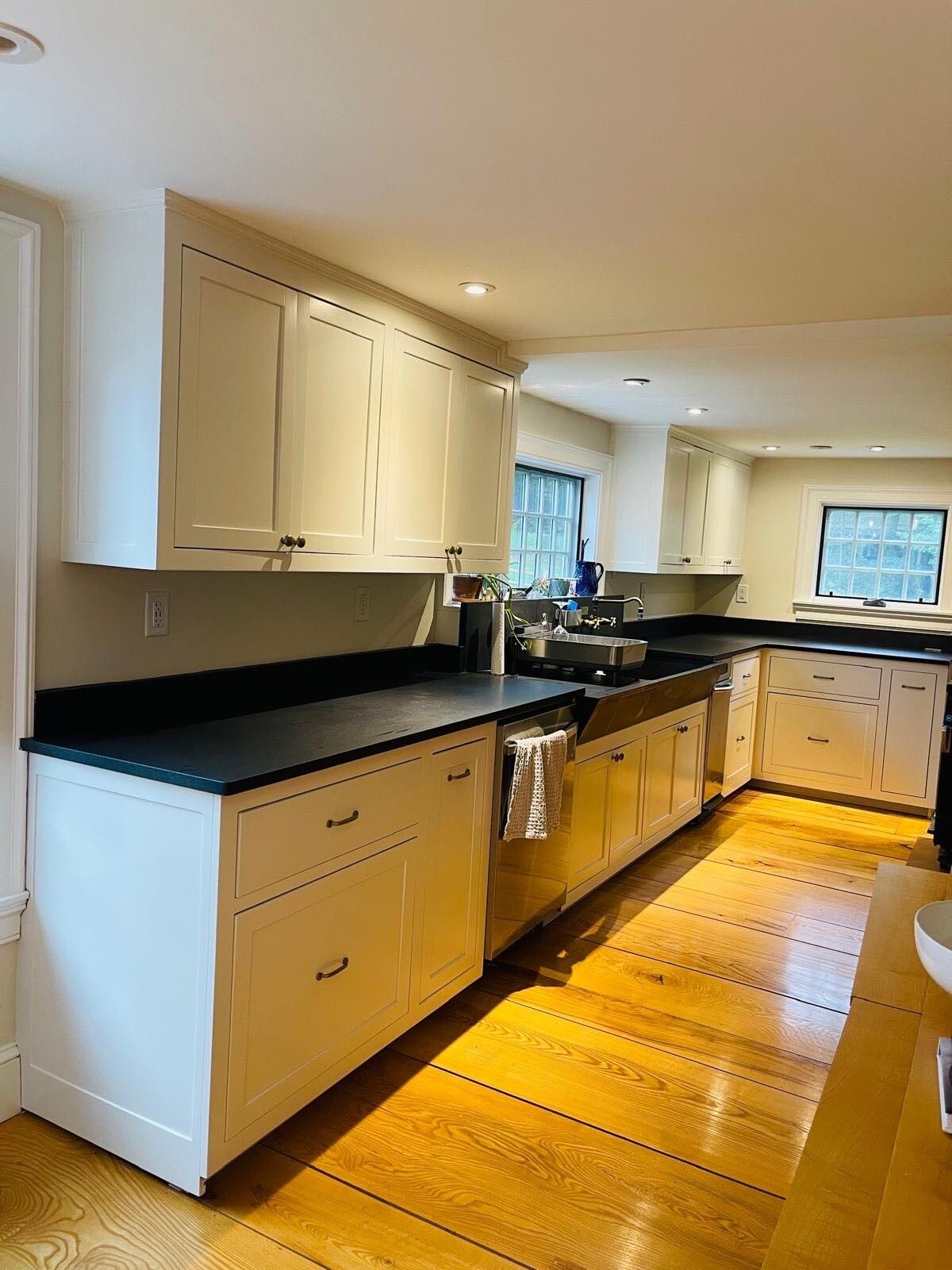 Completed custom off-white painted kitchen cabinets with soapstone countertops, bronze pulls, and warm wide-plank wood floors