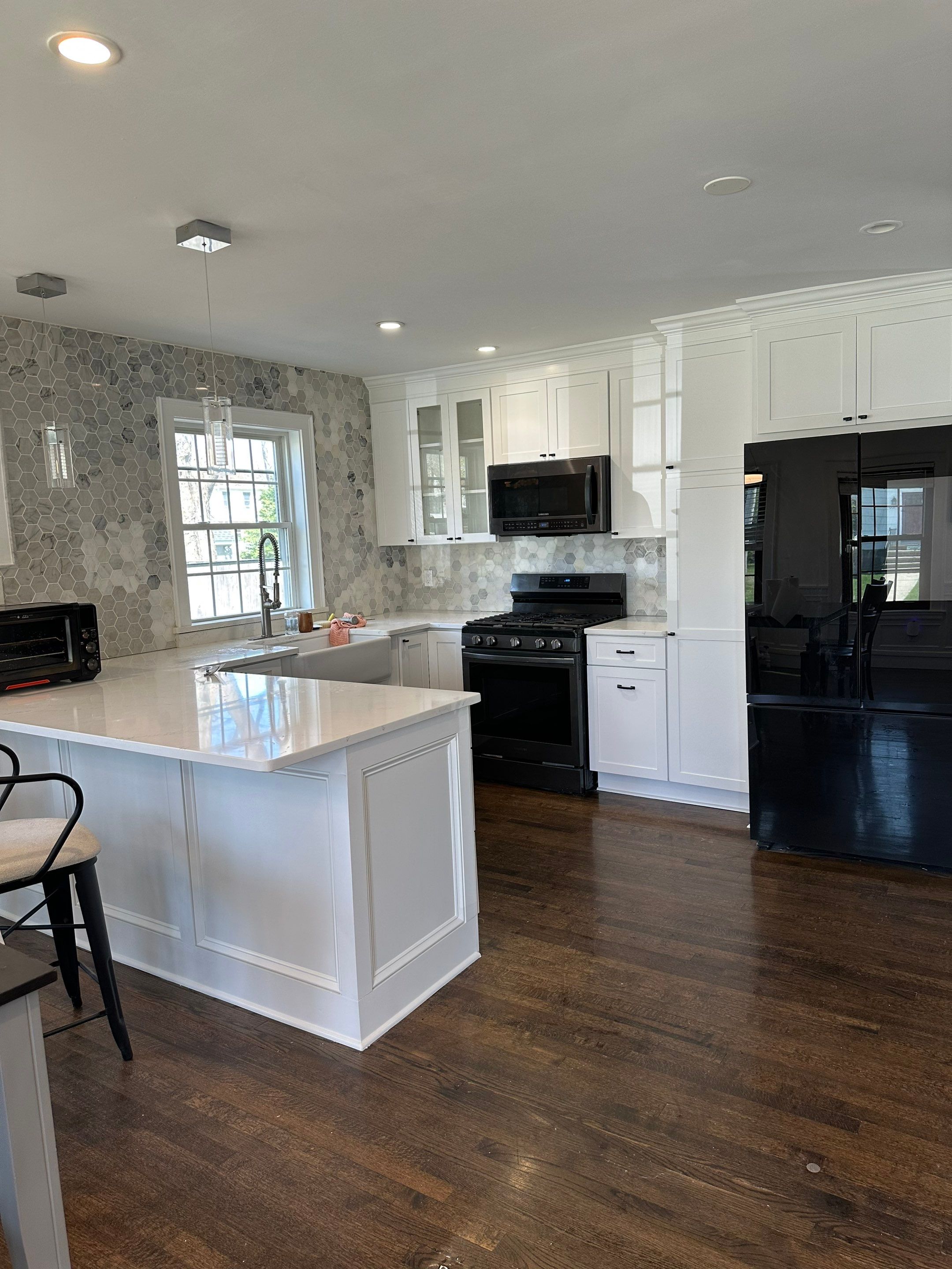 Completed crisp white painted kitchen cabinets with glass upper display doors, polished quartz peninsula, and marble hexagon tile backsplash