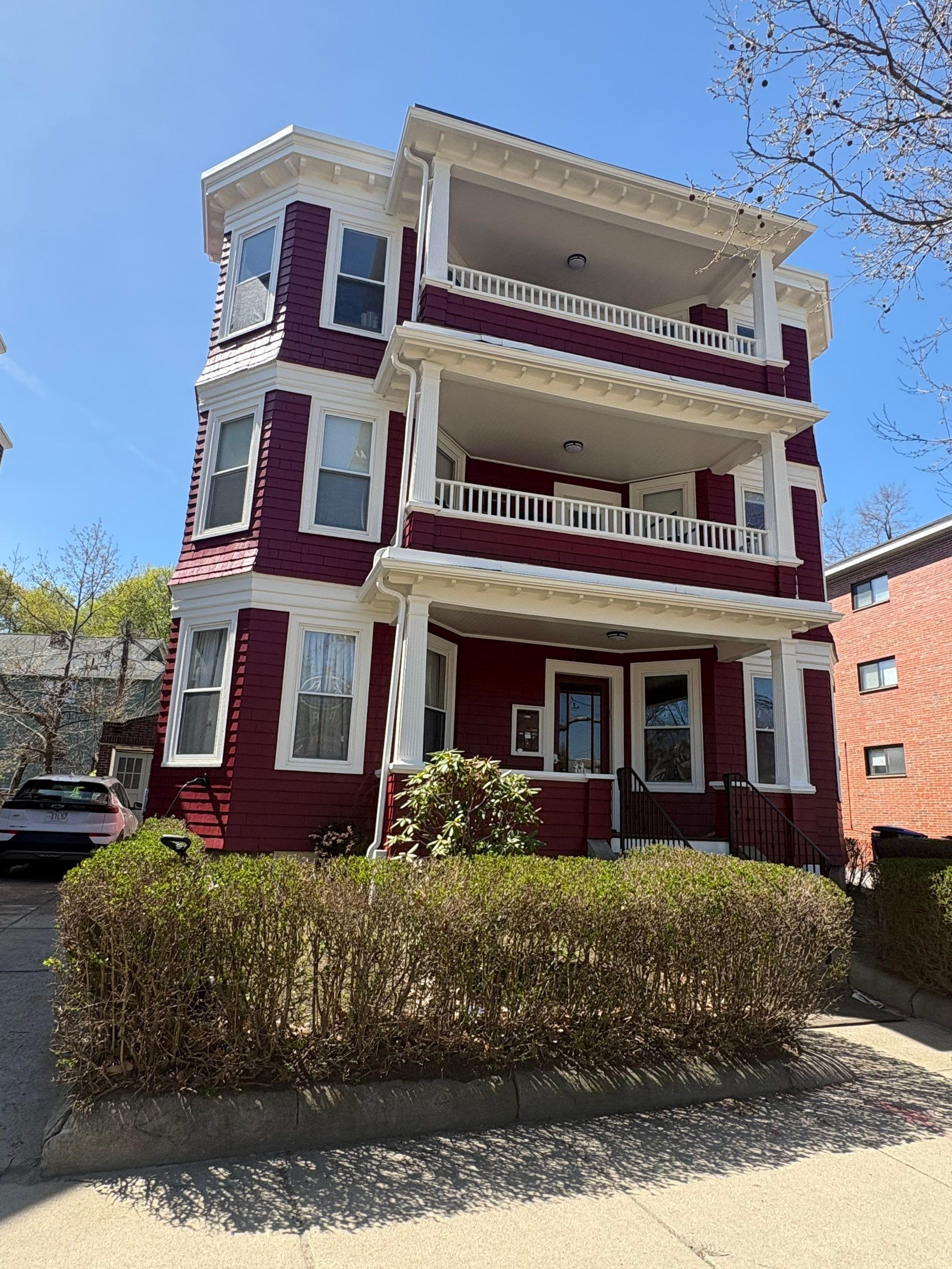 After painting: vibrant rich burgundy red three-story home with bright white architectural railings, columns, and trim