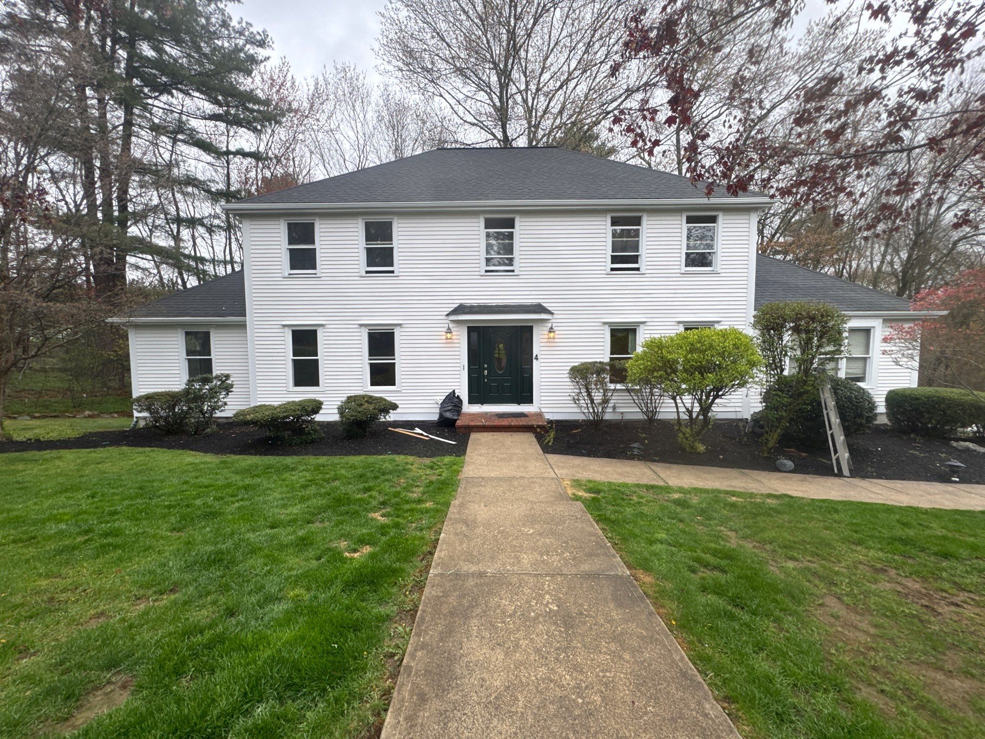 Completed exterior repaint of a two-story Massachusetts colonial with clean pure white siding and bold dark front door