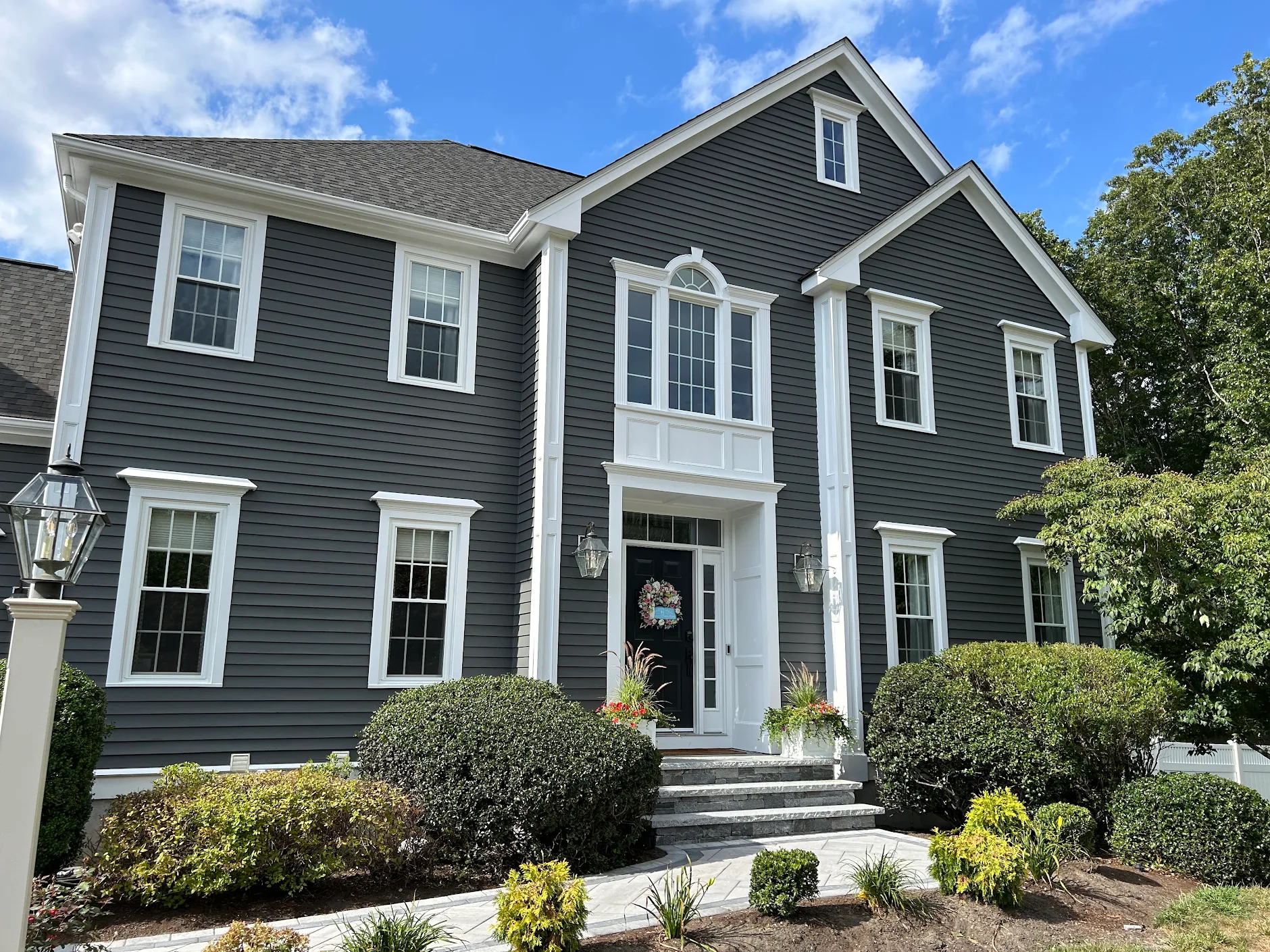 Completed exterior painting of a grand two-story colonial with deep charcoal grey siding, grand white front portico columns, and architectural trim