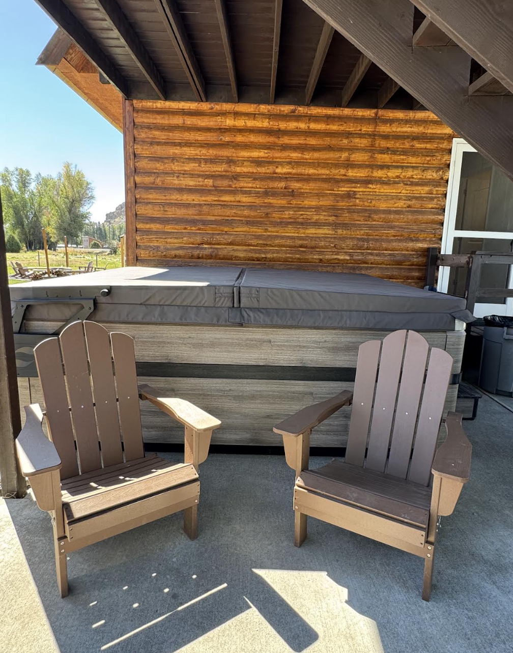 Covered hot tub patio with Adirondack chairs against log exterior